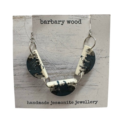 A necklace with three half moon resin shapes in blue with a black and white paint design held together with silver findings on a silver chain.