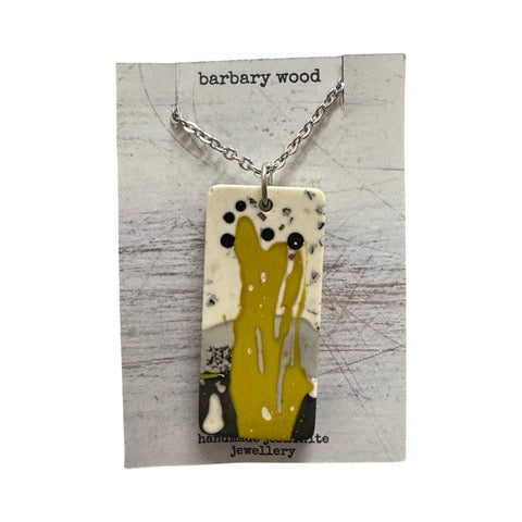 A rectangular pendant necklace iwith a muted paint design in mustard, black, grey and white on a silver chain.