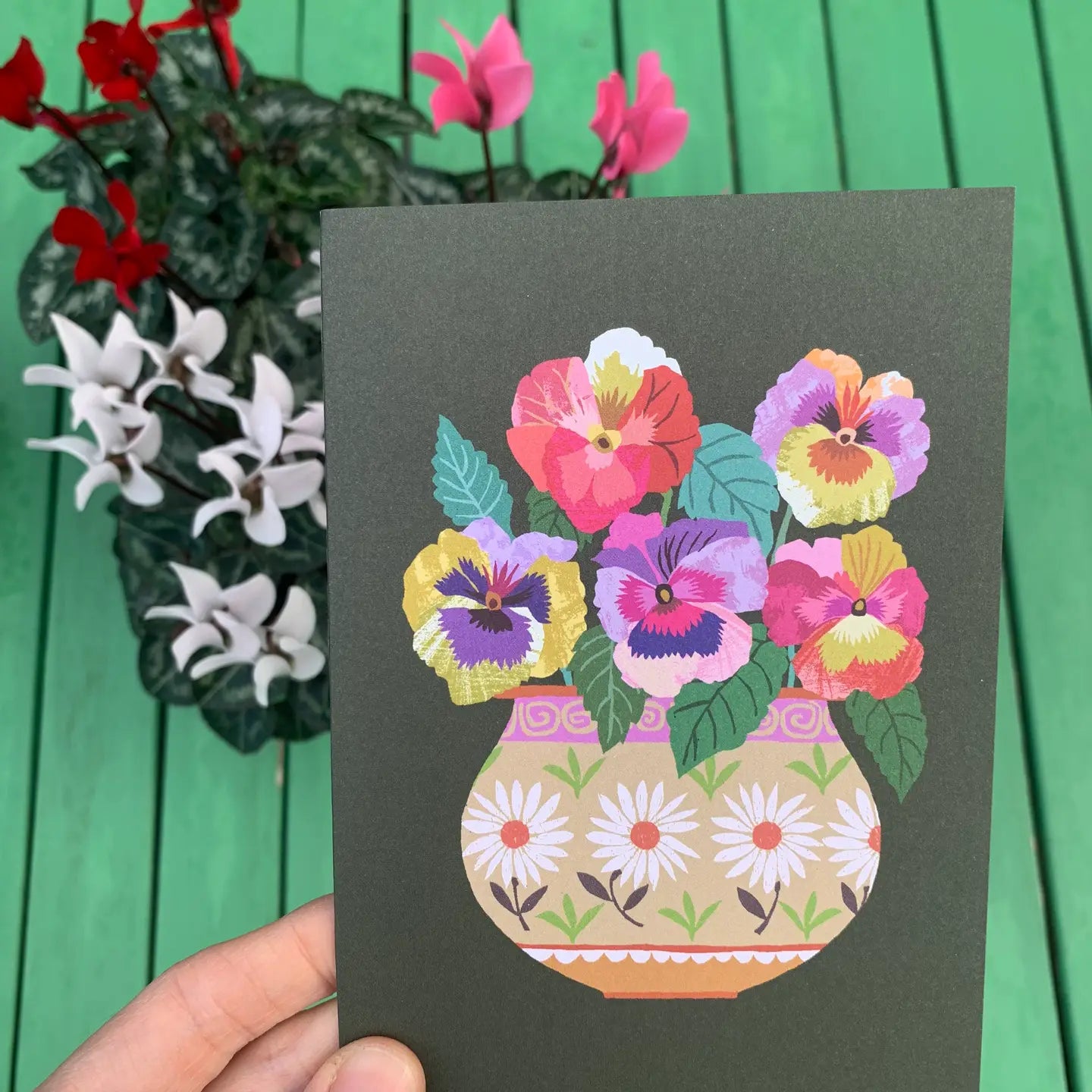 Card with a colorful floral design held against a green background with flowers.