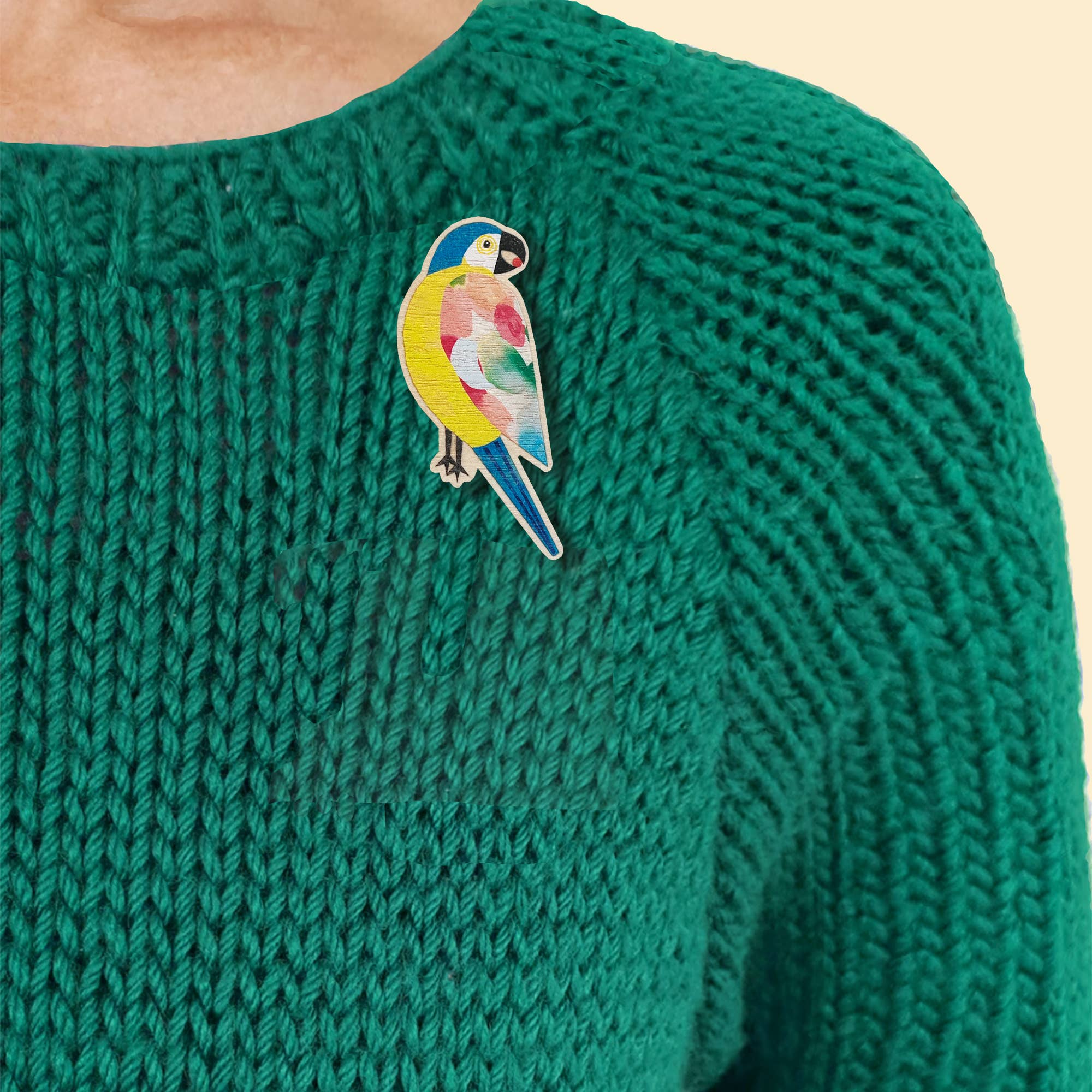 A colourful parrot pin badge, pinned onto the chest of a person wearing a textured green knit sweater.