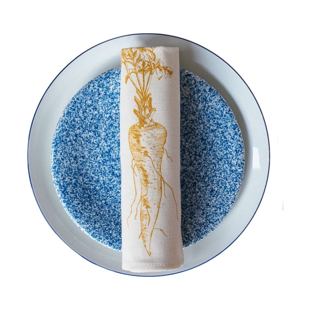 Cream cotton napkin with a mustard parsnip rolled on a plate.