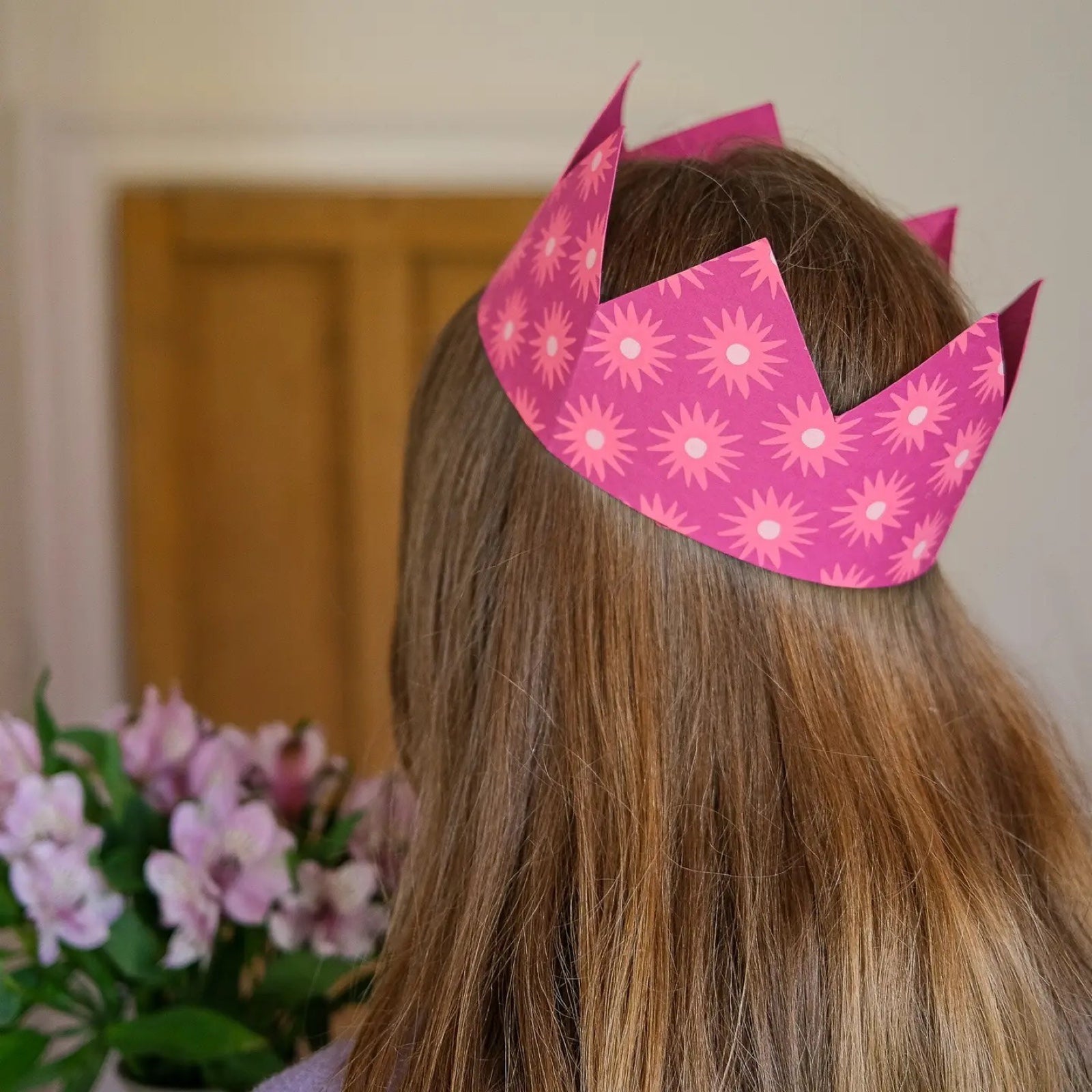 A pink party crown being worn on a girls head.