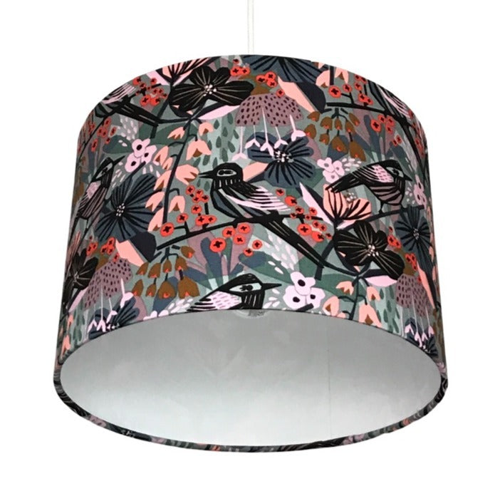 Close up of a drum lampshade covered in canvas fabric with black birds in a pastel pink, blue and grey floral background.