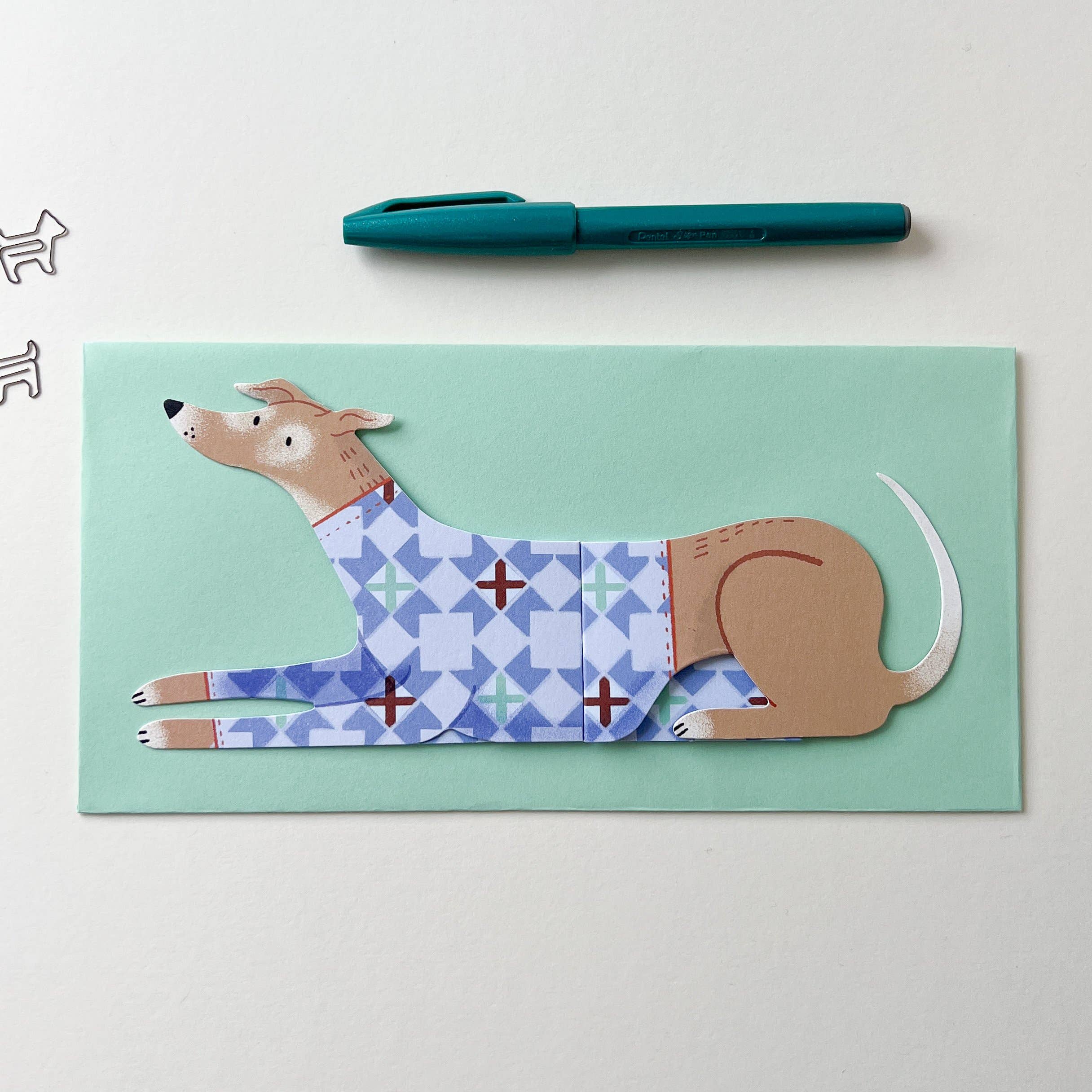 Card with a dog illustration on a light green background, sat on a table next to a pen.
