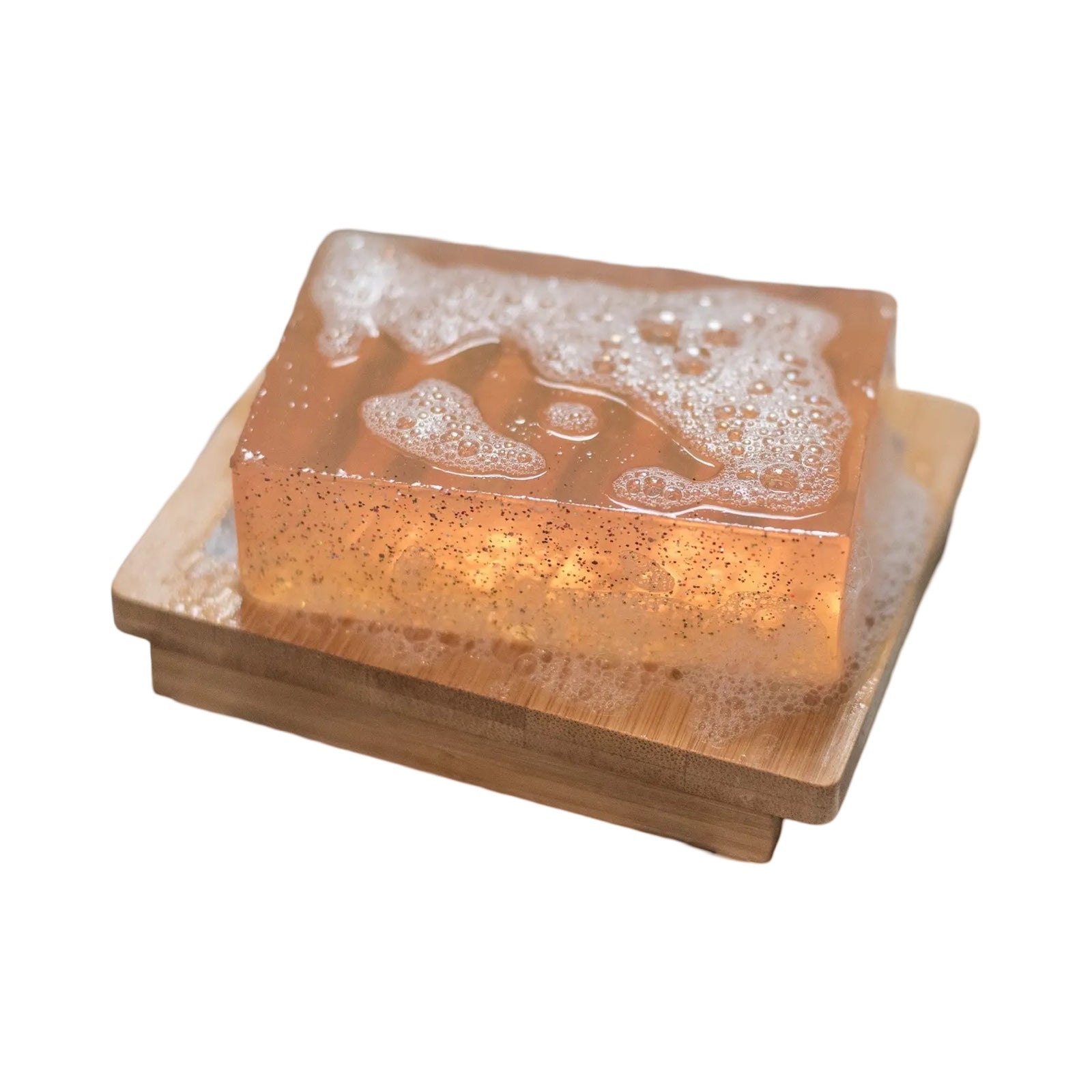 A bar of pale orange peach bellini soap sitting on a wooden soap dish.