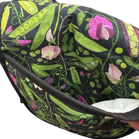 Oven gloves featuring green, yellow and purple pods of peas with pink flowers and green foliage on a black background.