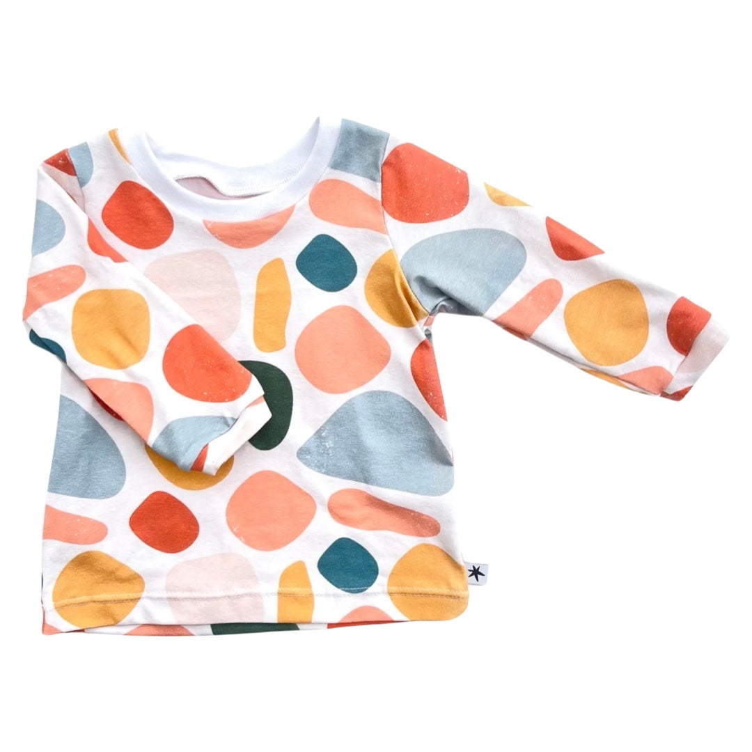 A long-sleeved baby t-shirt with a colorful pebble pattern in various shades of pink, blue, green, and orange.