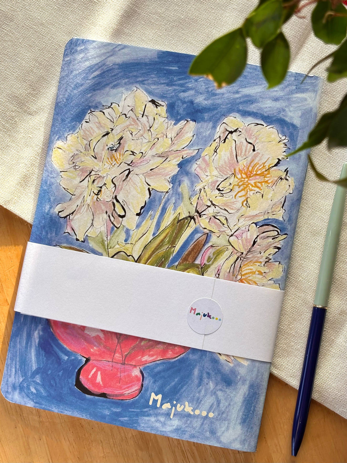 A square hardcover notebook with a painted floral cover design, wrapped with a white band. The cover features blue watercolour background with cream and pink peony-like flowers and a red flower at the bottom.