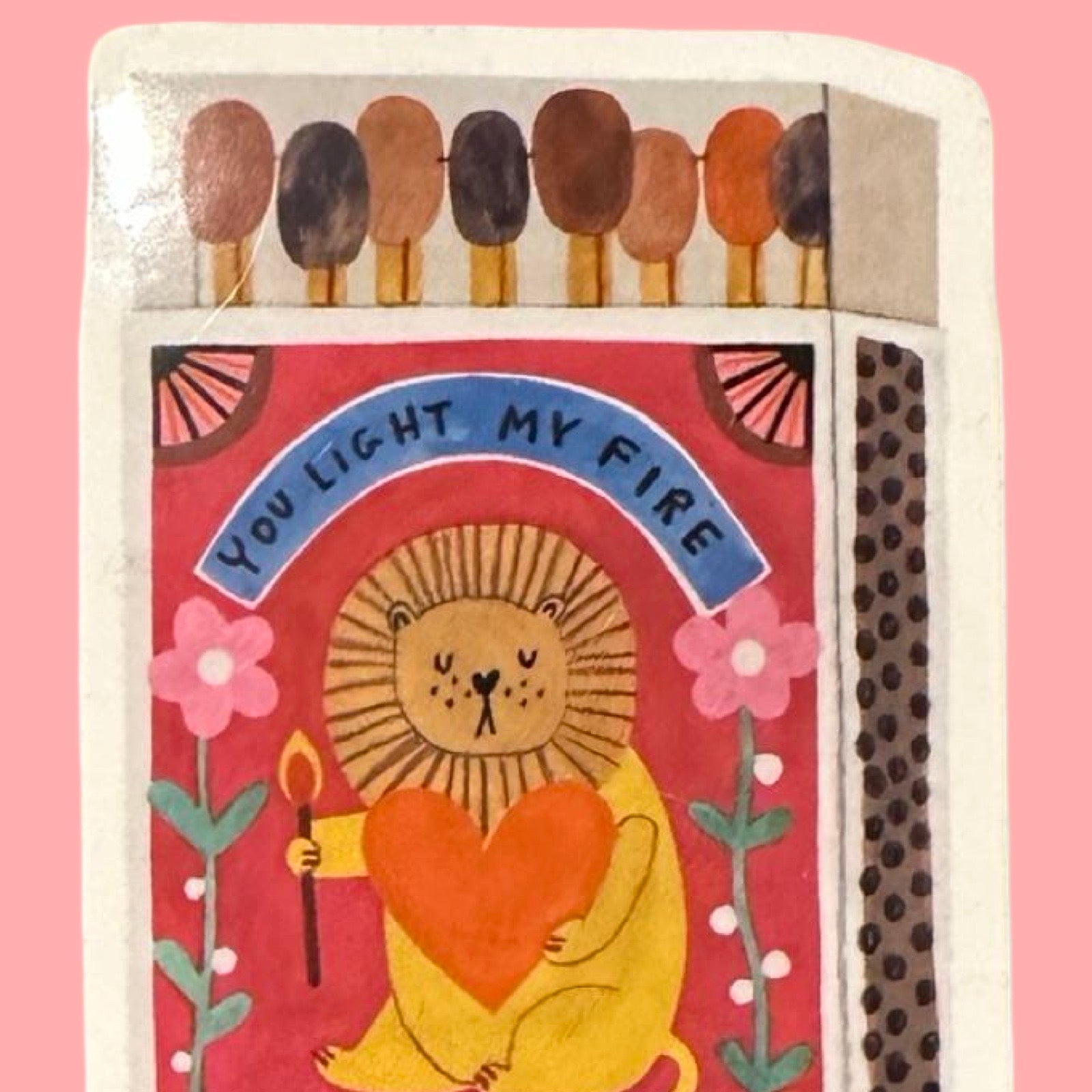 Matchbox with a lion holding a heart and 'You Light My Fire' text on a pink background.