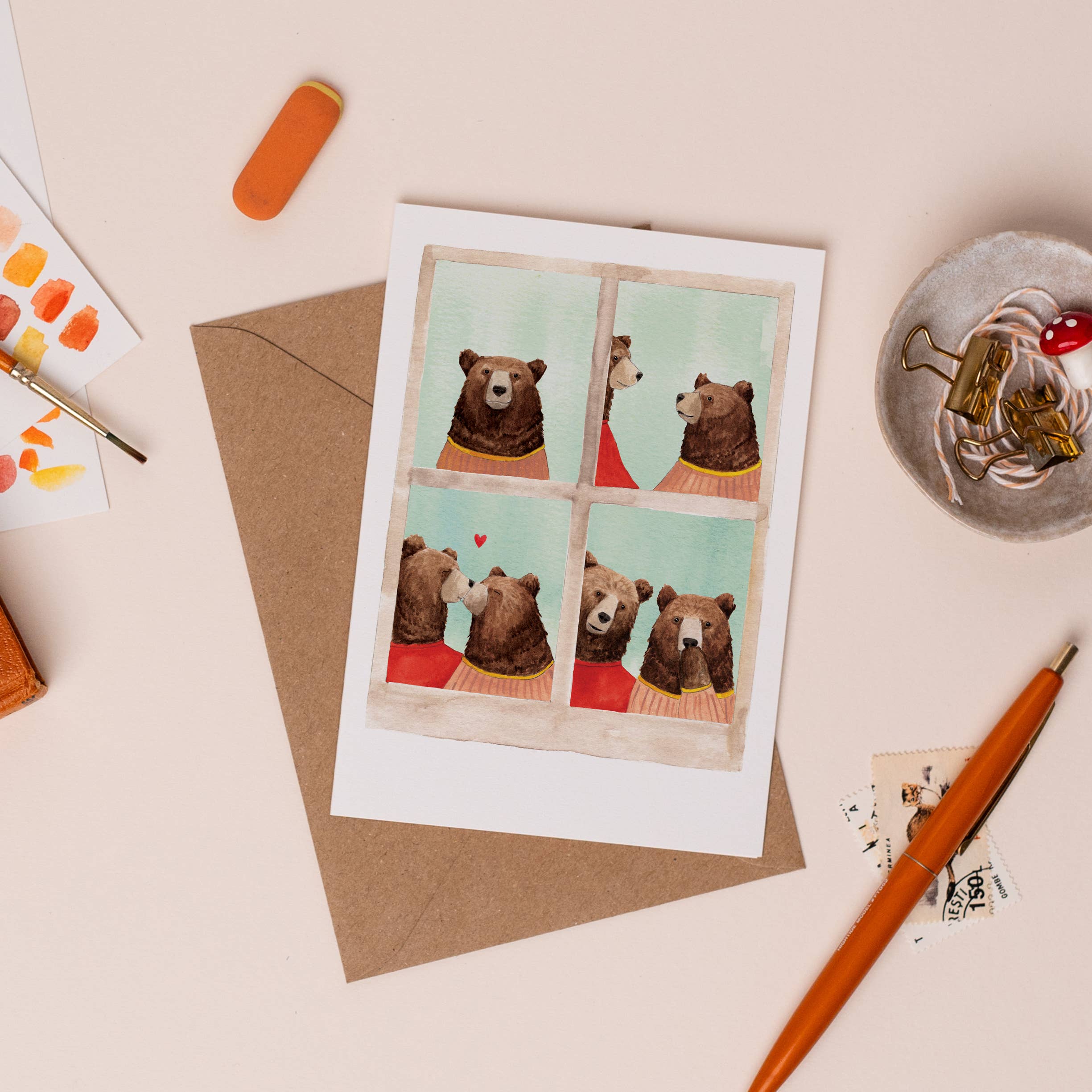 Greeting card with bear illustrations on a desk with stationery items.