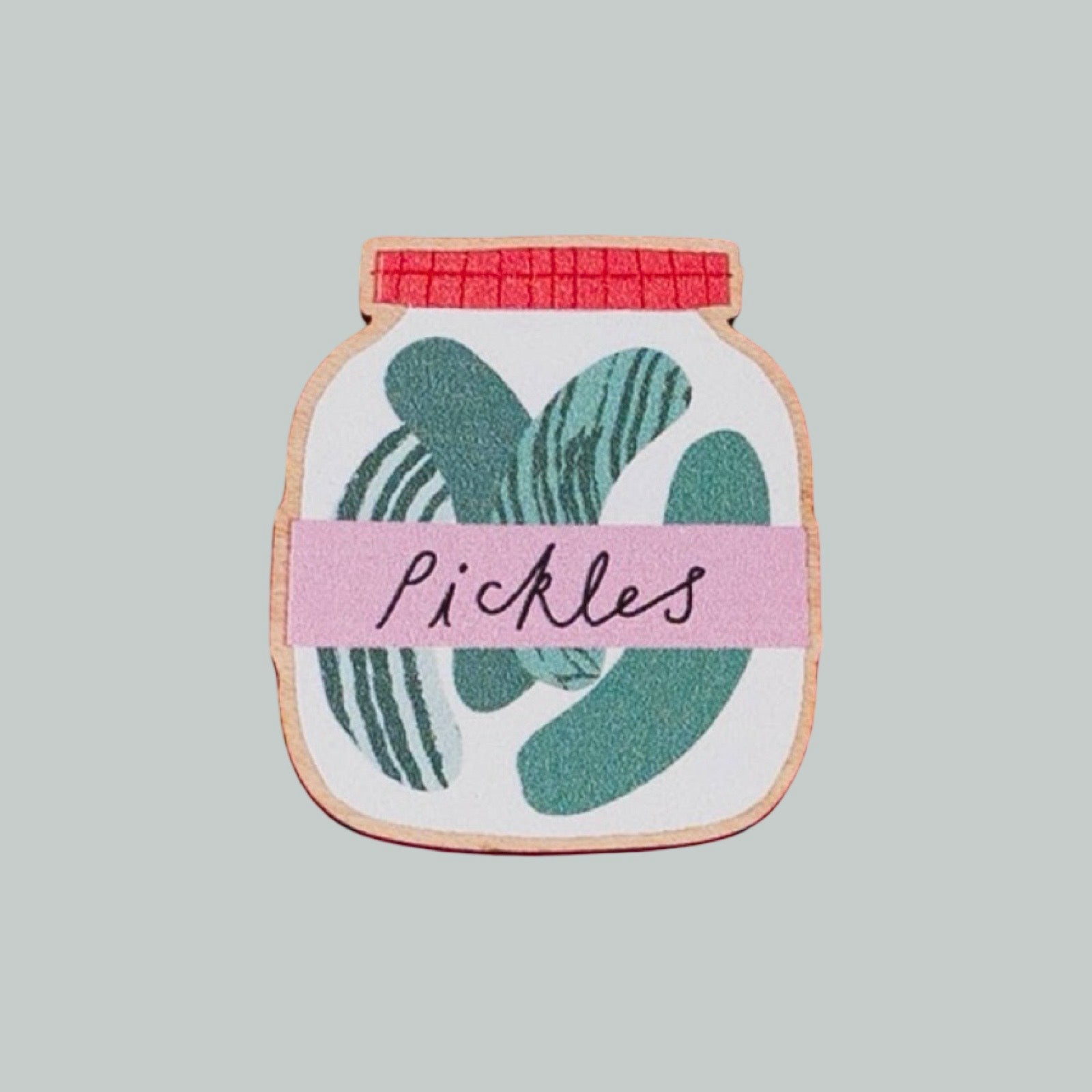 A jar-shaped decorative item with a pink label reading 'Pickles' and green pickle spear illustrations, shown on a plain light green background.
