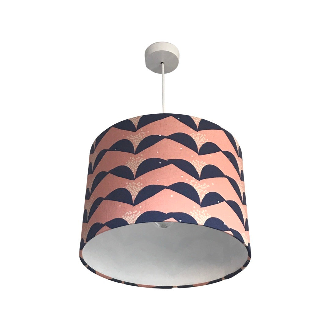A cylindrical lampshade with a pink background and navy blue abstract floral pattern.