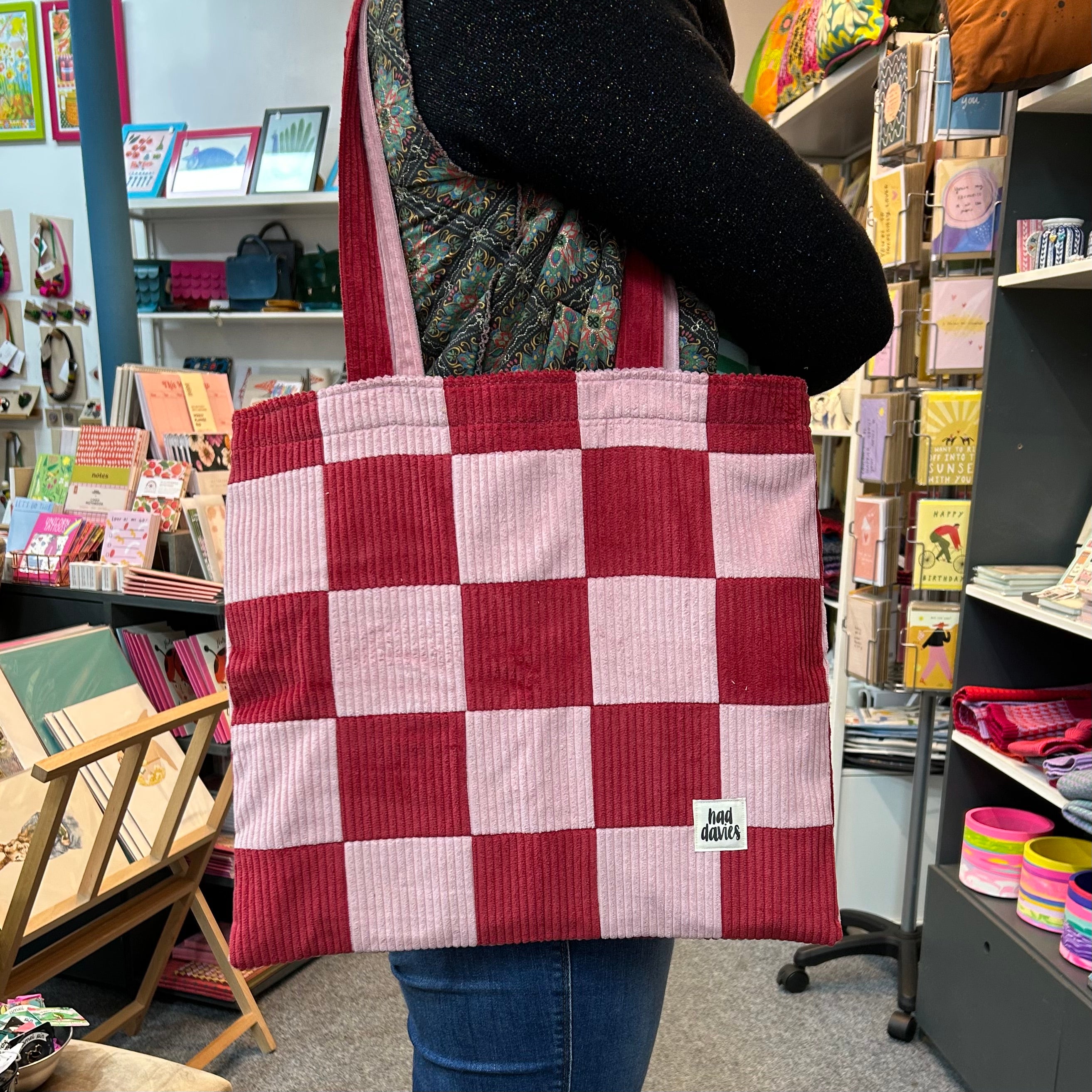 Person holding a red and pink checkered tote bag in a store setting.