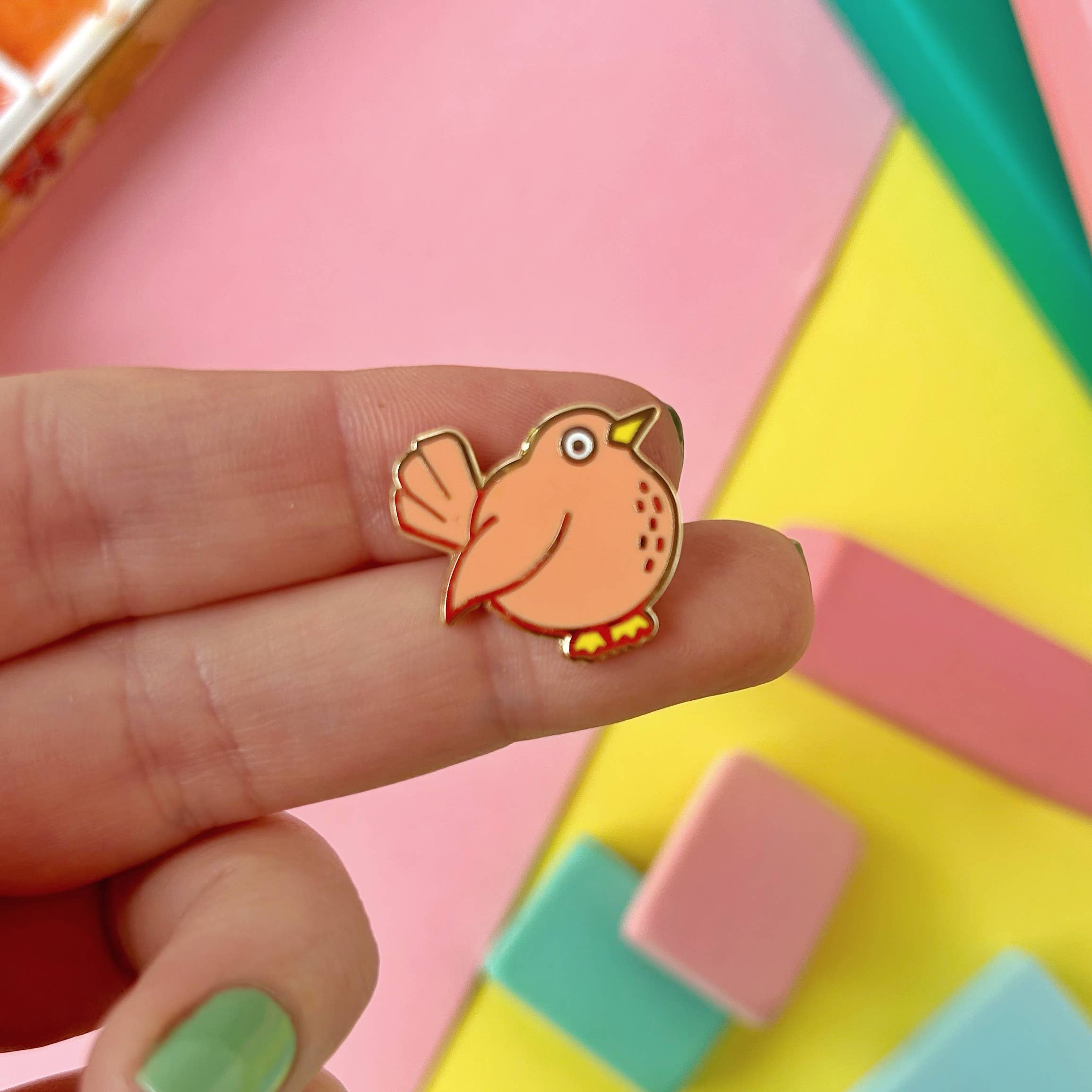 Bird-shaped pin held between fingers against a colorful geometric background.