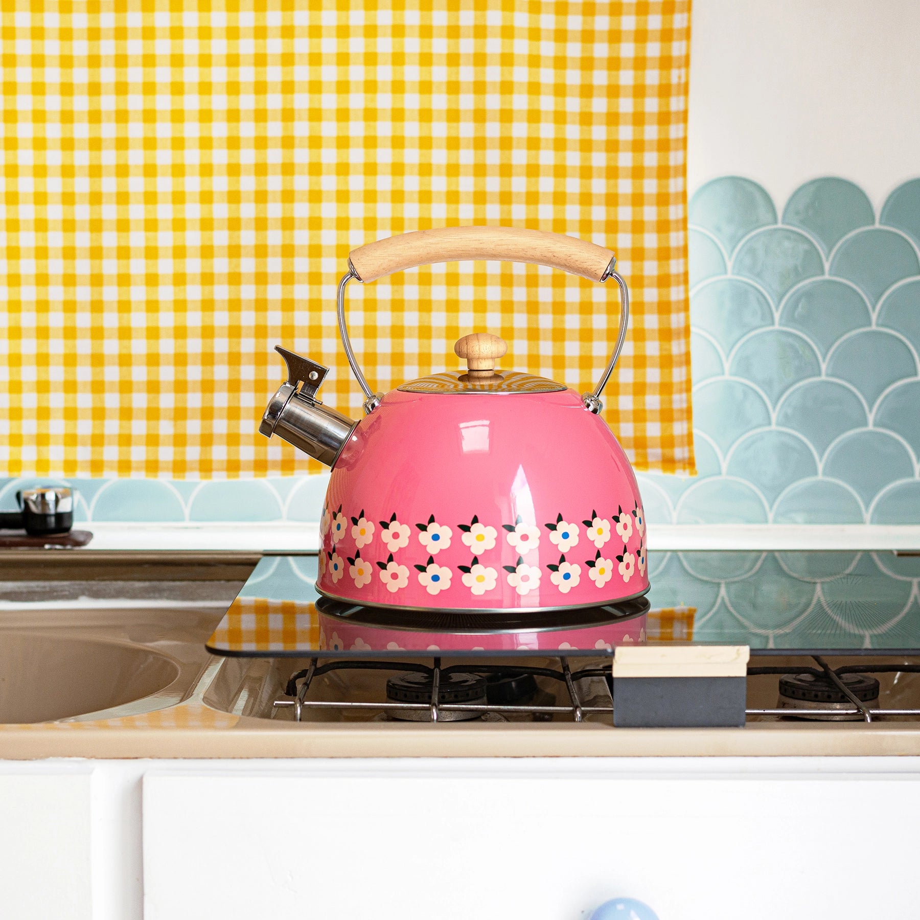 Pink floral-patterned kettle on a stove with a yellow checkered tea towel in the background.