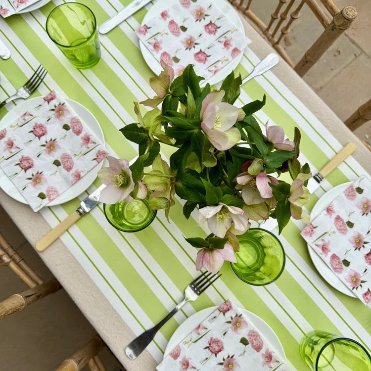 Dining table set with floral plates, green glasses, and a centerpiece of pink and green flowers on a striped tablecloth.