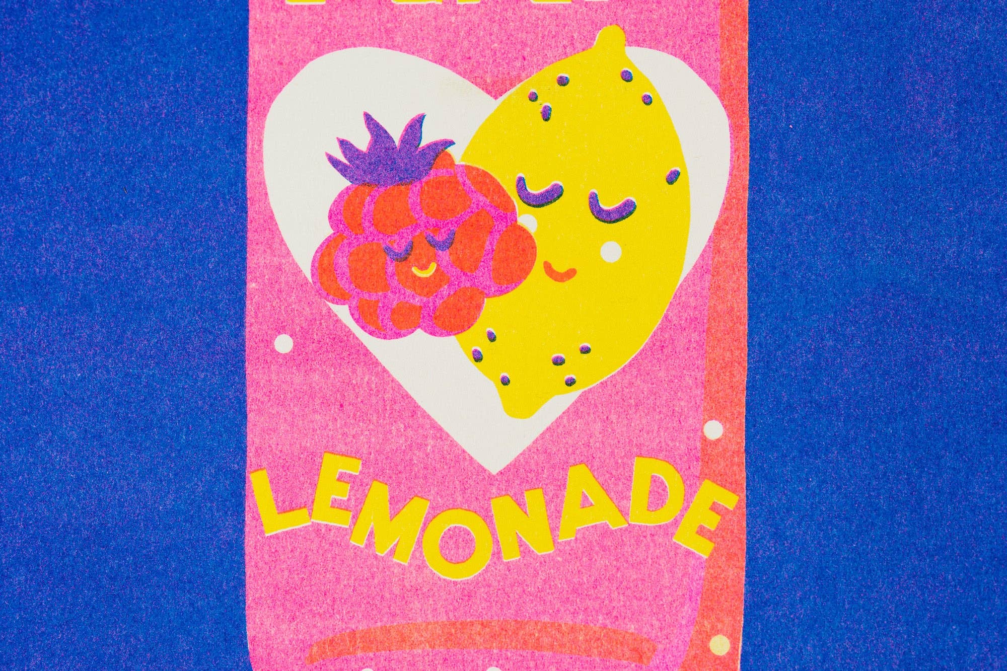 A close-up of a colourful printed design featuring a pink heart-shaped label with a yellow lemon and a red raspberry illustration, with the word 'LEMONADE' in yellow text, set against a blue background.