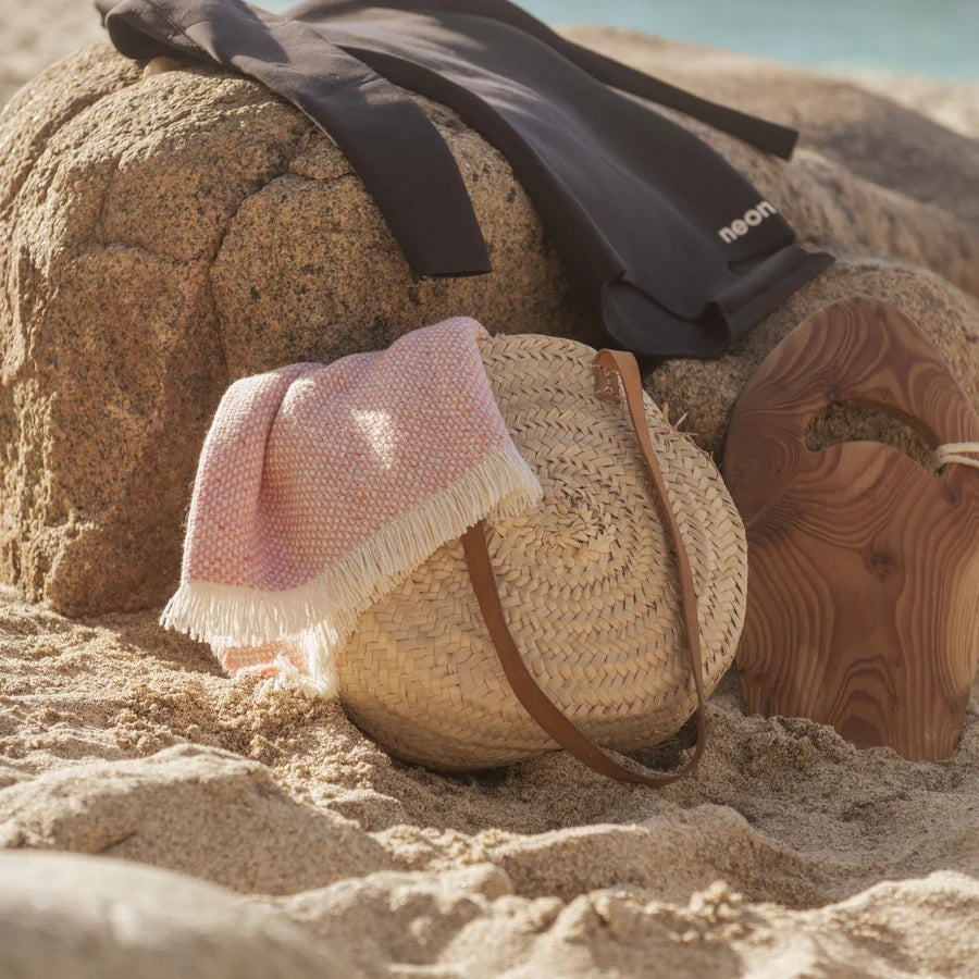 Woven bag with pink blanket on a beach.