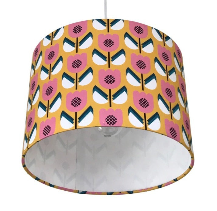Close up of a drum lampshade covered in cotton retro-inspired fabric with a mustard background and pink, white and blue flowers.