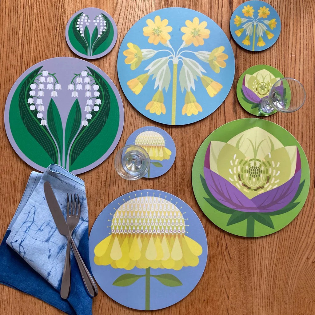 A round placemat featuring a cowslip flower abstract design in blue and yellow on a laid table.