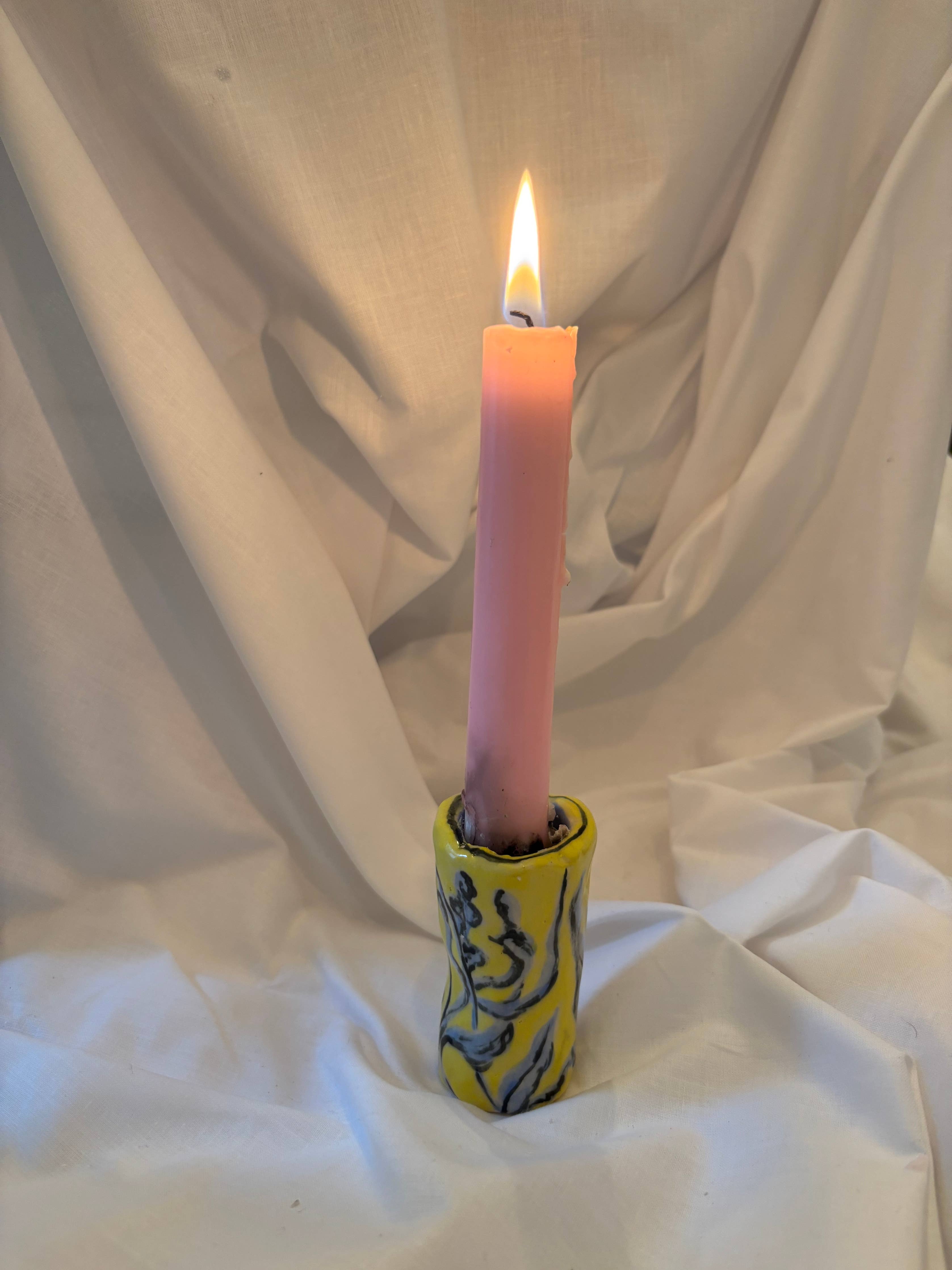 Pink candle in a yellow holder on a white fabric background.