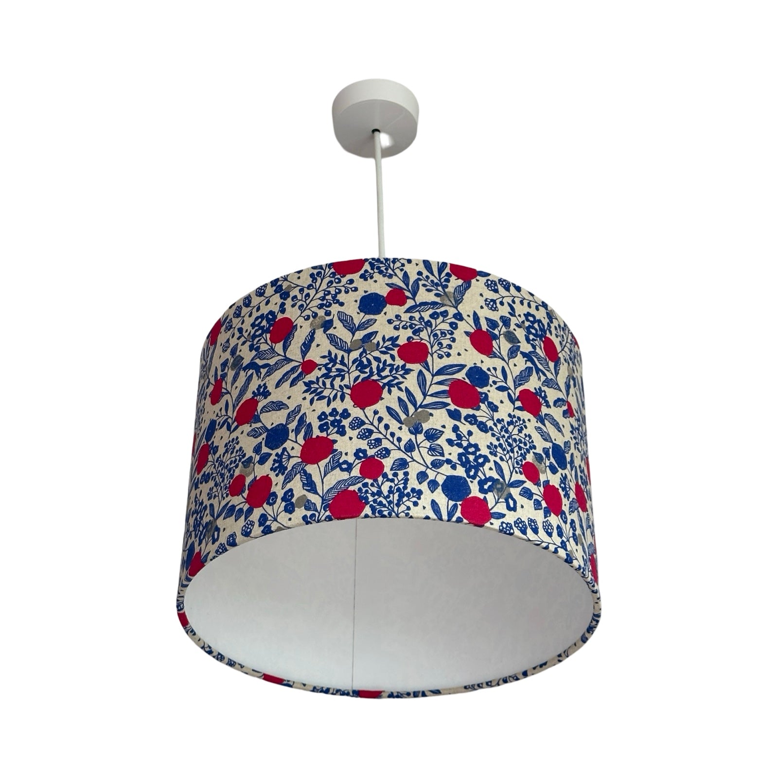 A drum lampshade covered in cream cotton fabric with pink plums, grey circles, blue foliage and blue foxes.