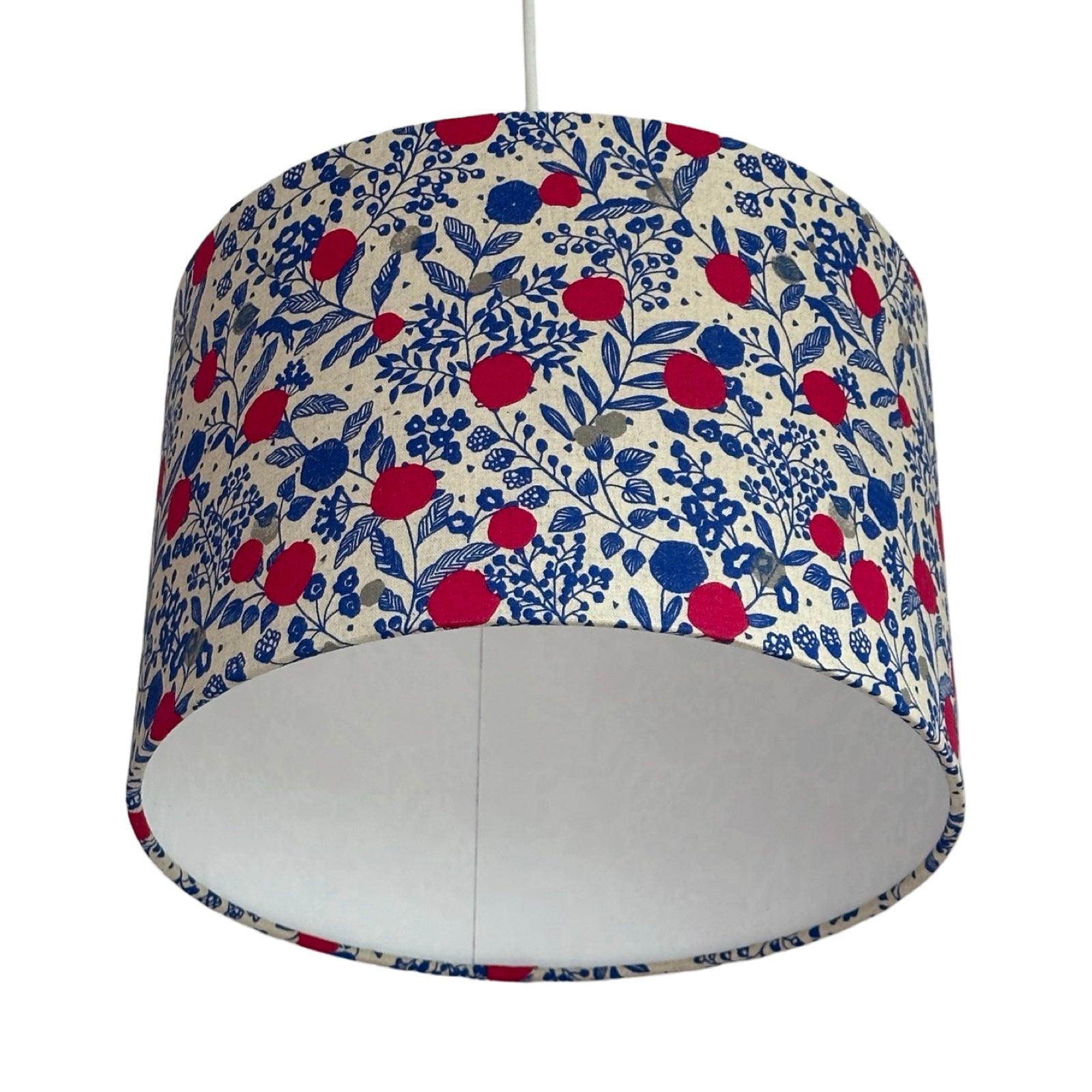A drum lampshade covered in cream cotton fabric with pink plums, grey circles, blue foliage and blue foxes.