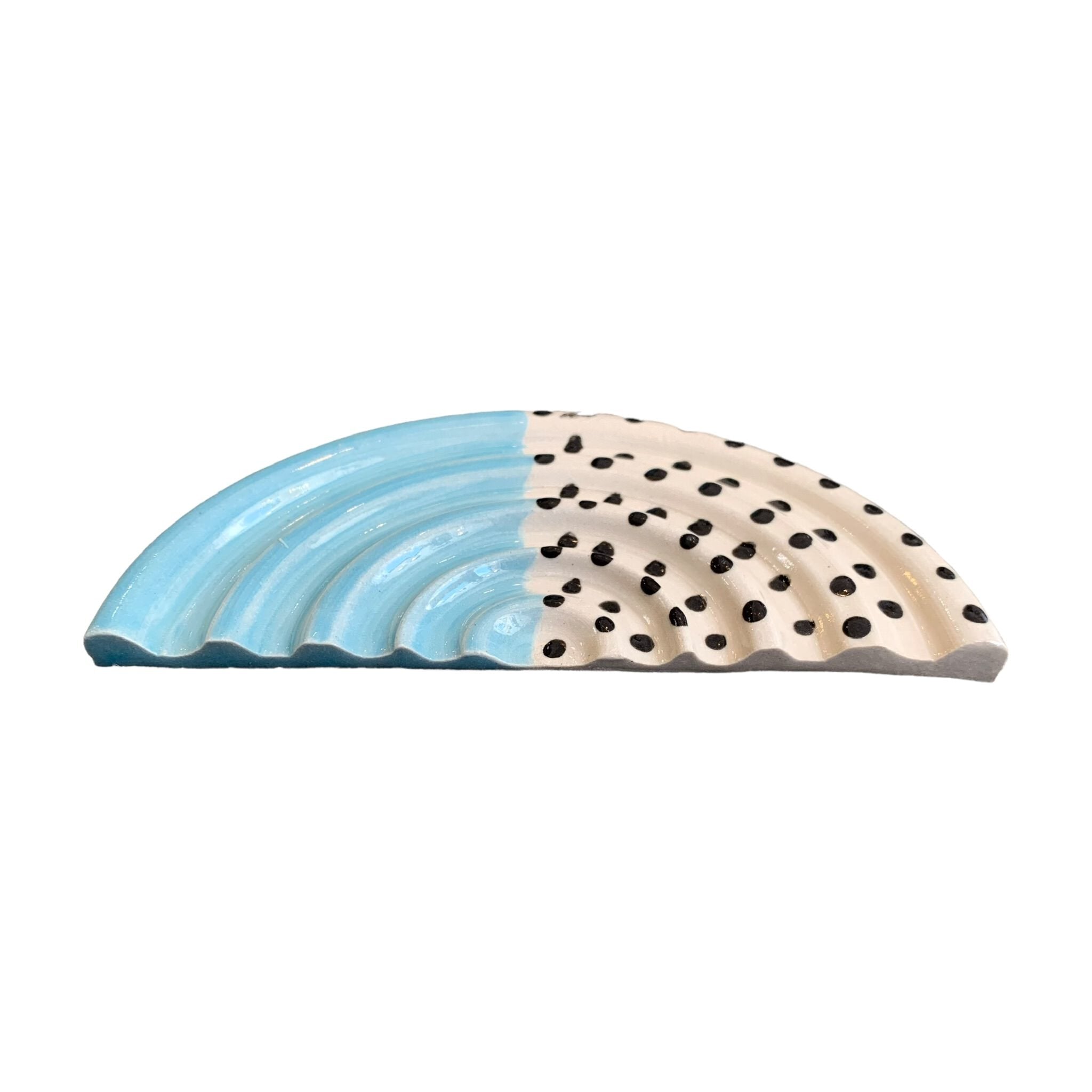 An arc-shaped ceramic soap dish, one half is pale blue and the other half is white with black polka dots.
