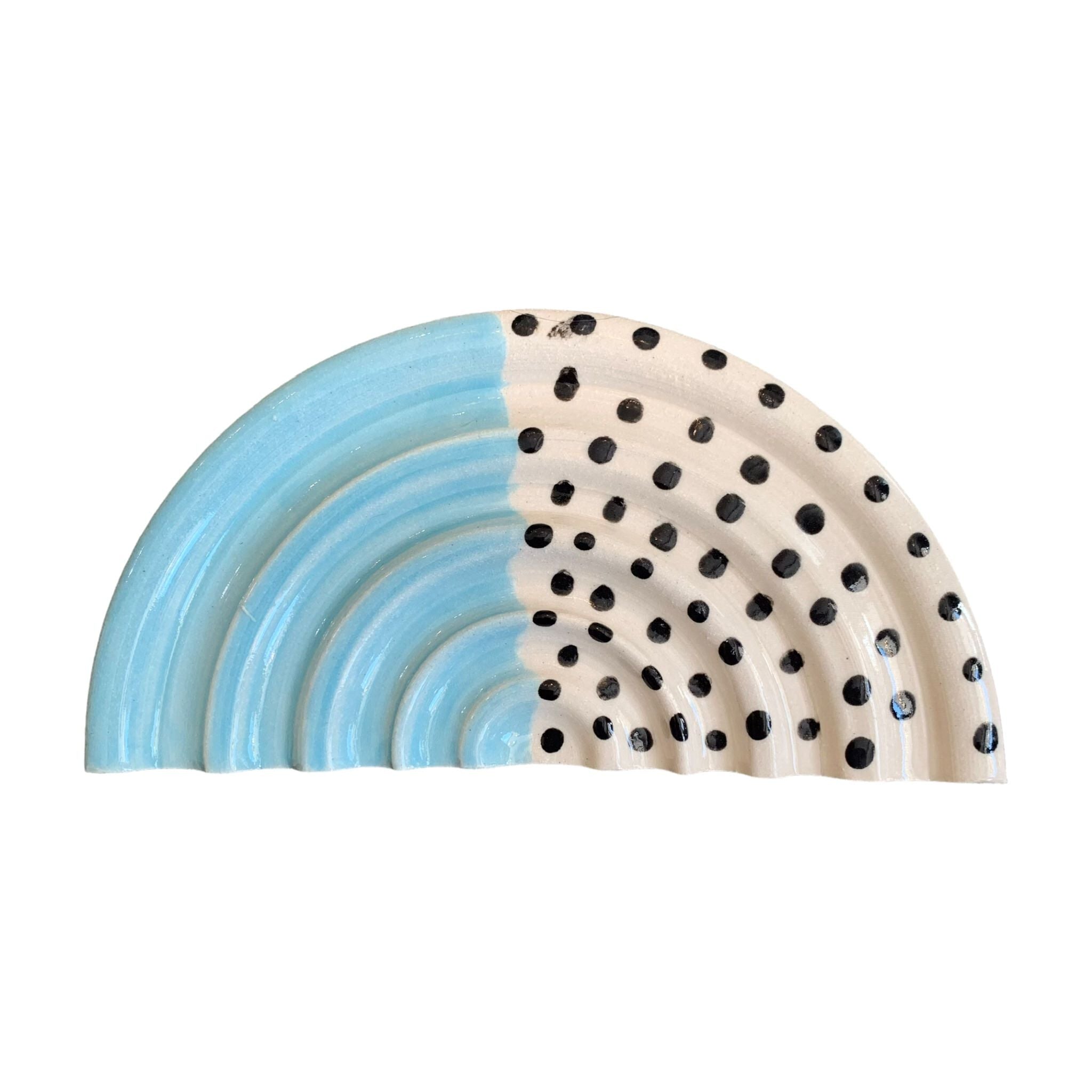 An arc-shaped ceramic soap dish, one half is pale blue and the other half is white with black polka dots.