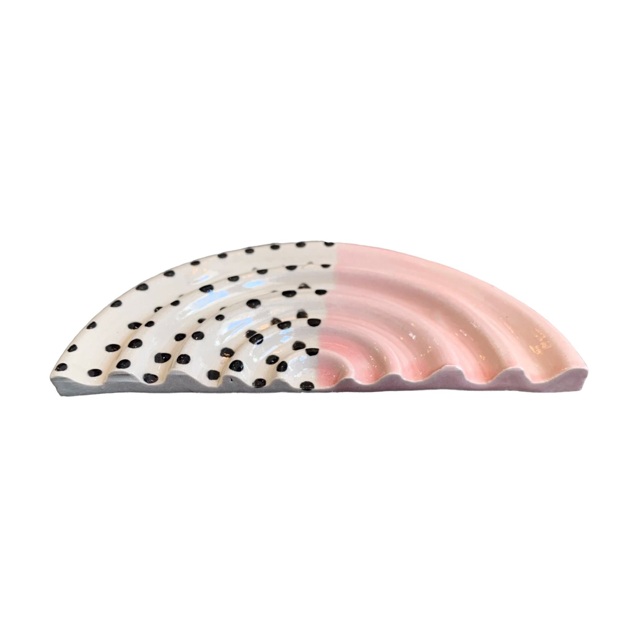 An arc-shaped ceramic soap dish, one half is pale pink and the other half is white with black polka dots.