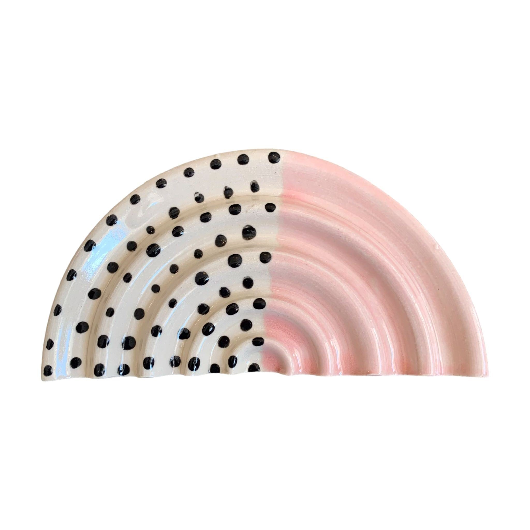An arc-shaped ceramic soap dish, one half is pale pink and the other half is white with black polka dots.