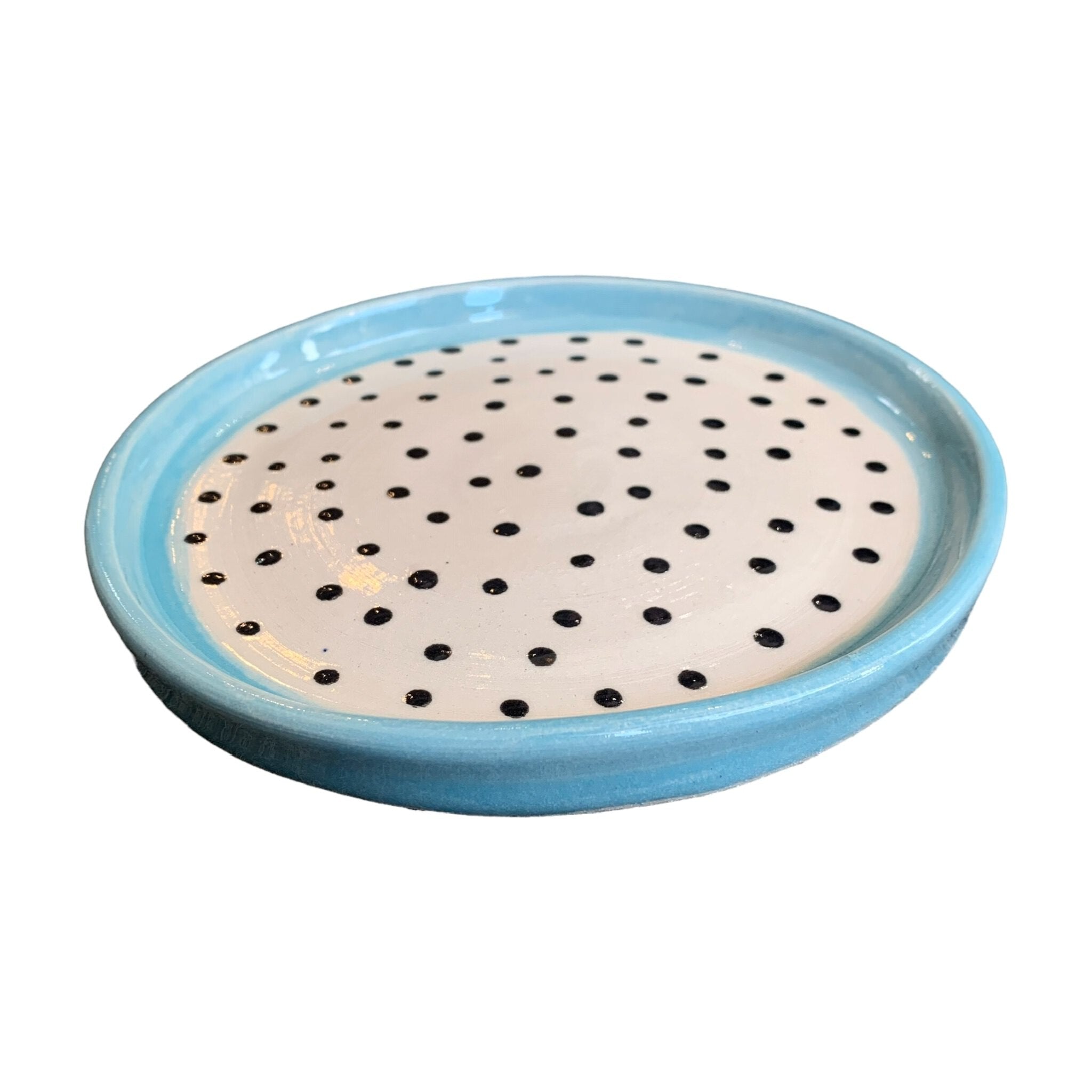 A ceramic trinket dish with a turquoise edge and white centre with black polka dots.
