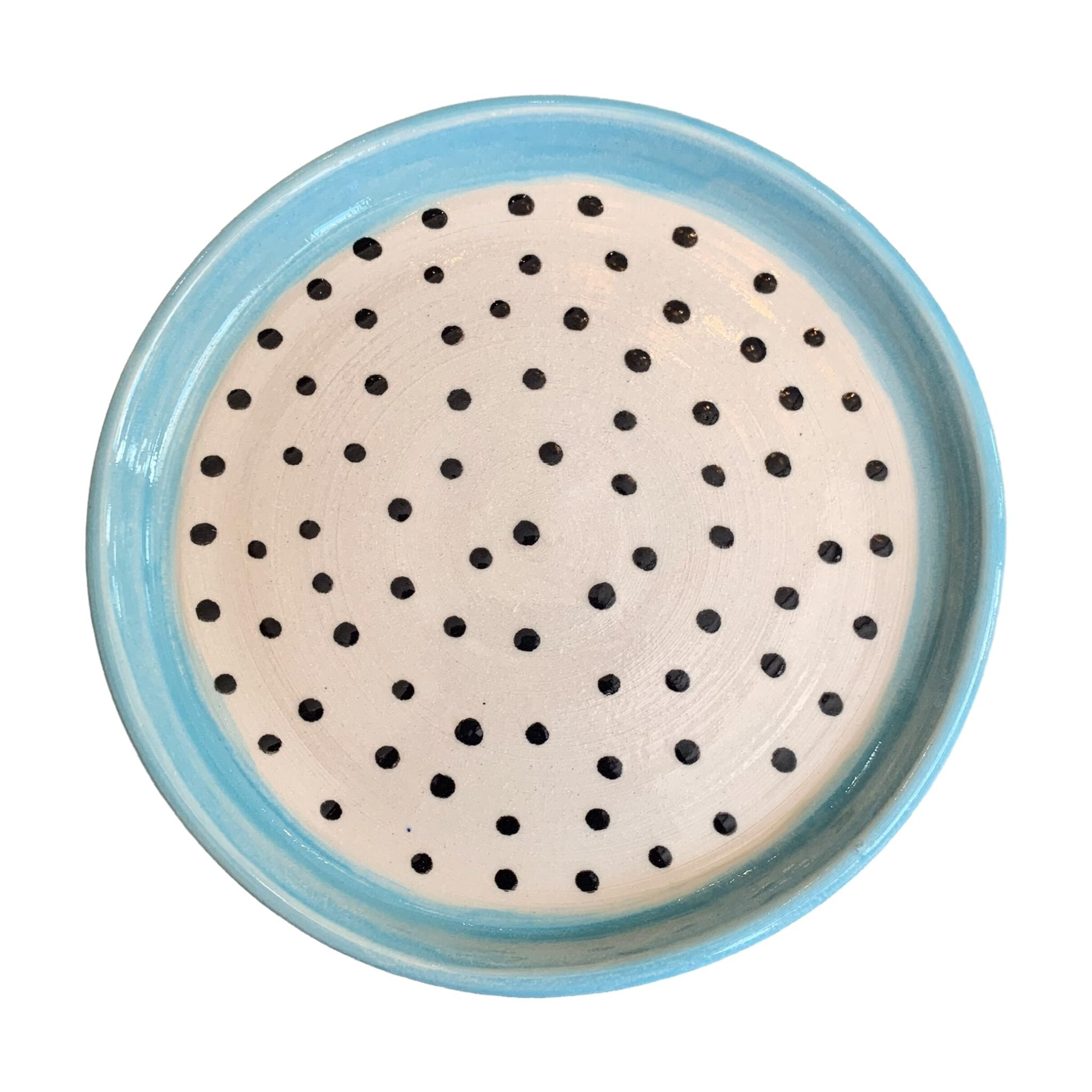 A ceramic trinket dish with a turquoise edge and white centre with black polka dots.