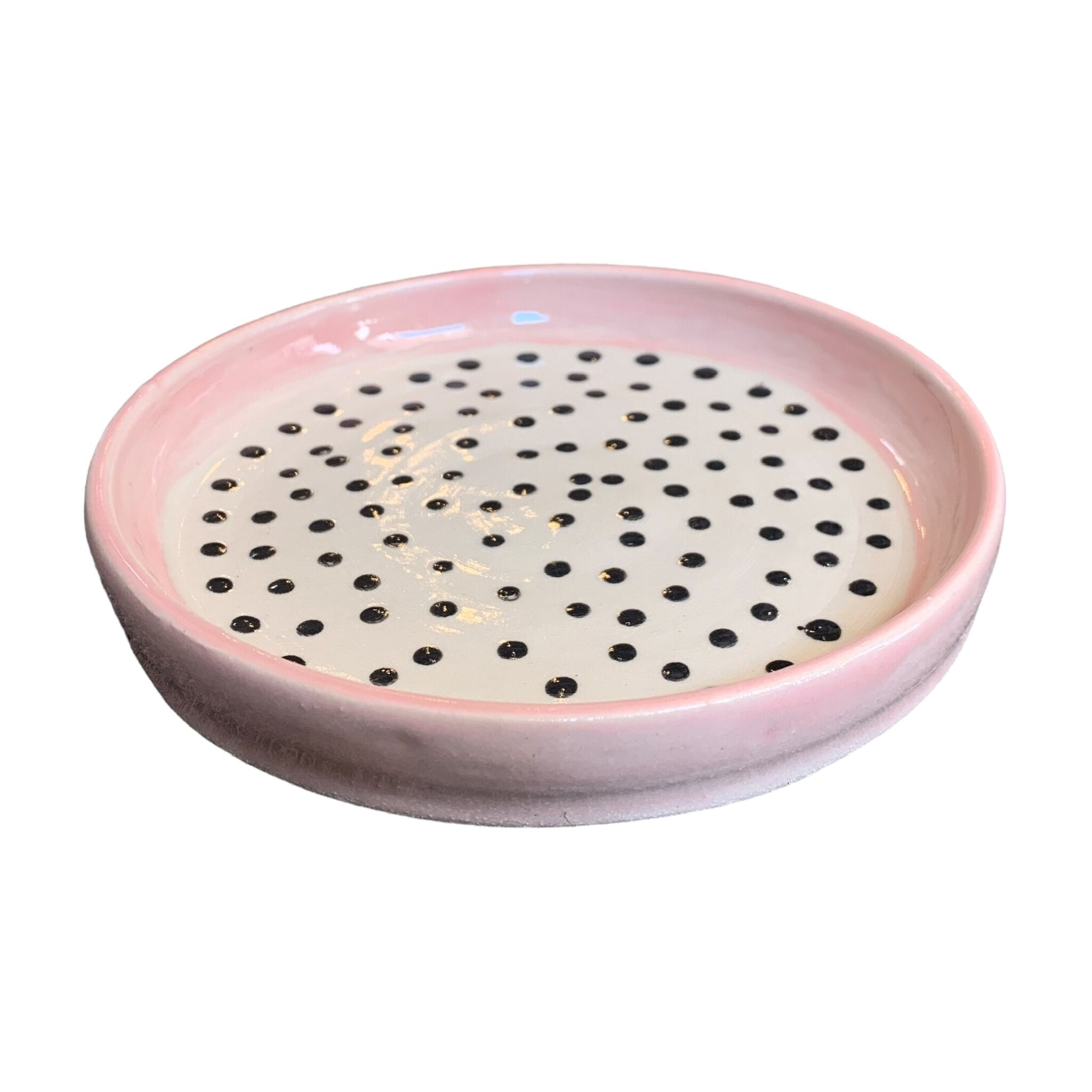 A ceramic trinket dish with a pink edge and white centre with black polka dots.