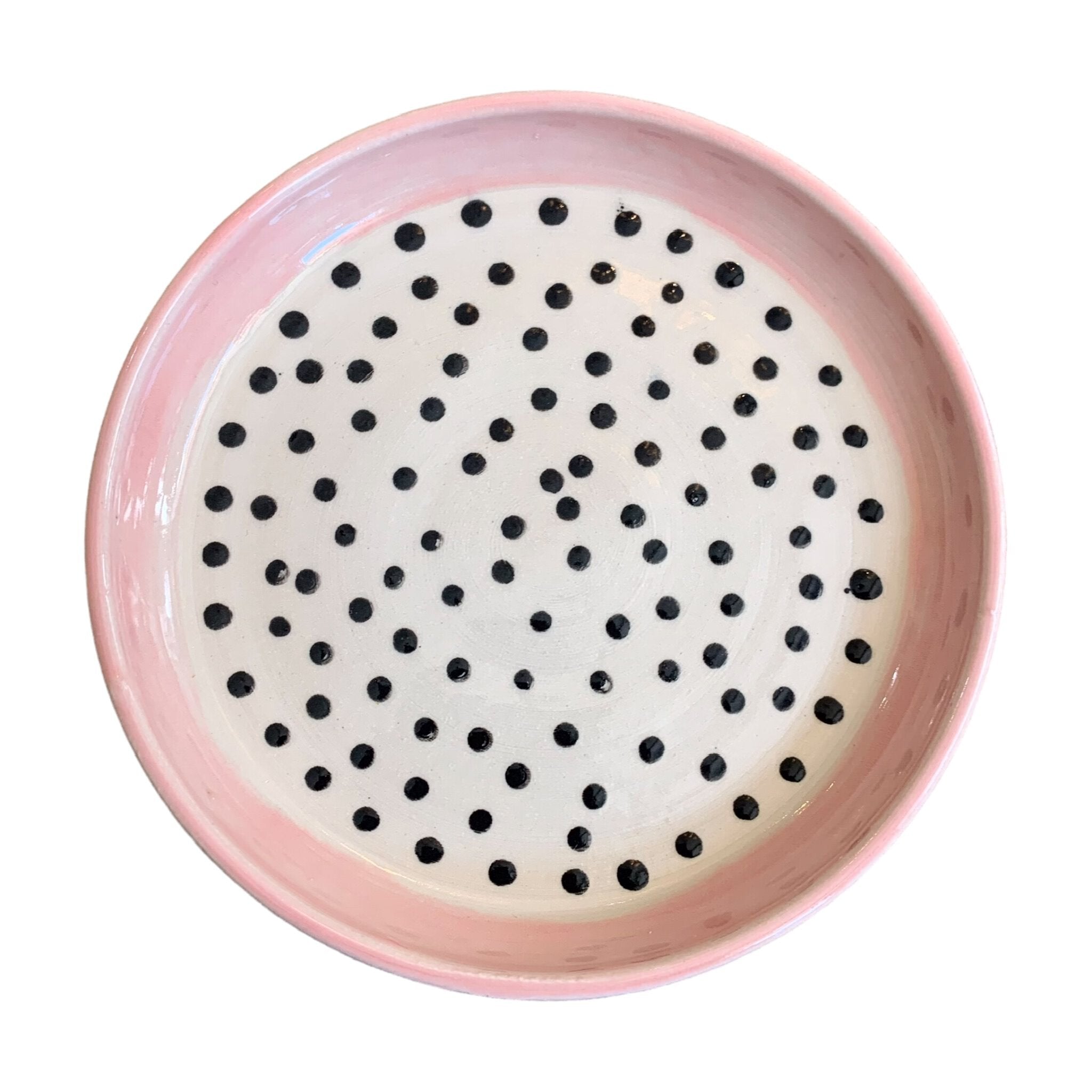 A ceramic trinket dish with a pink edge and white centre with black polka dots.
