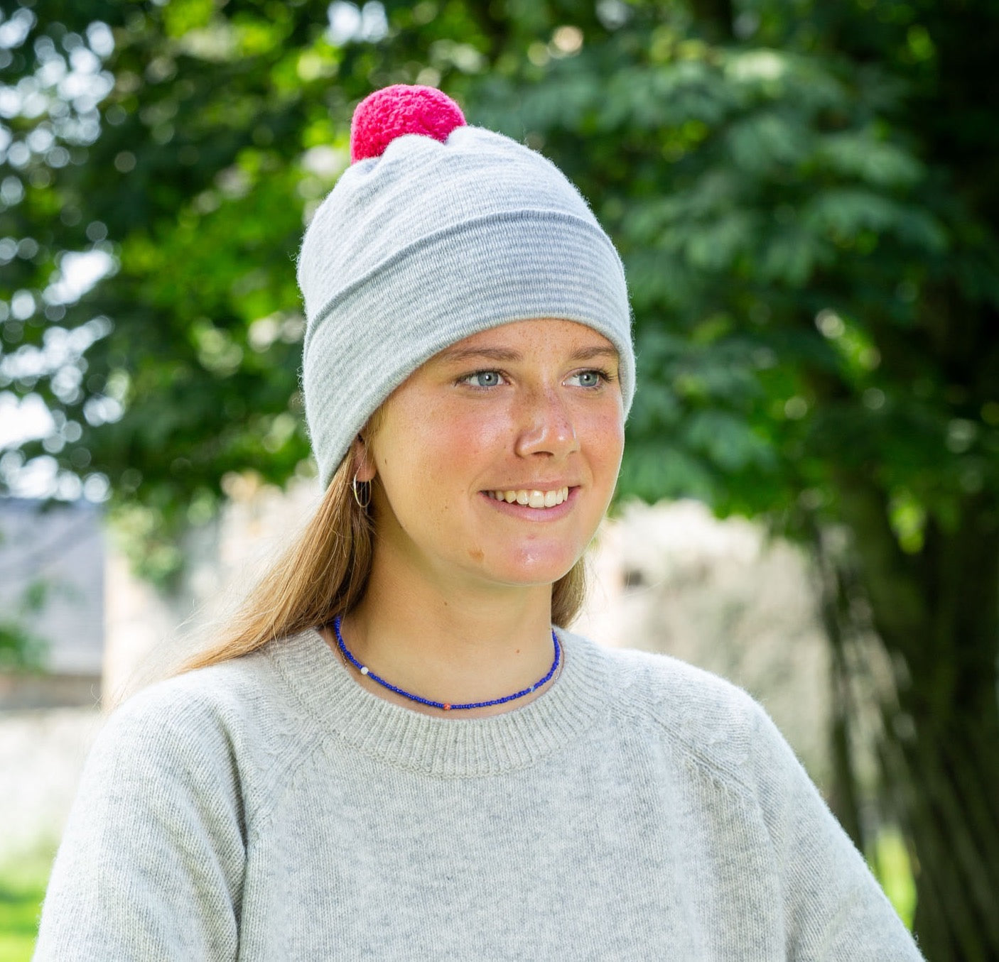 Person wearing a grey knit hat with a red pom-pom outdoors.