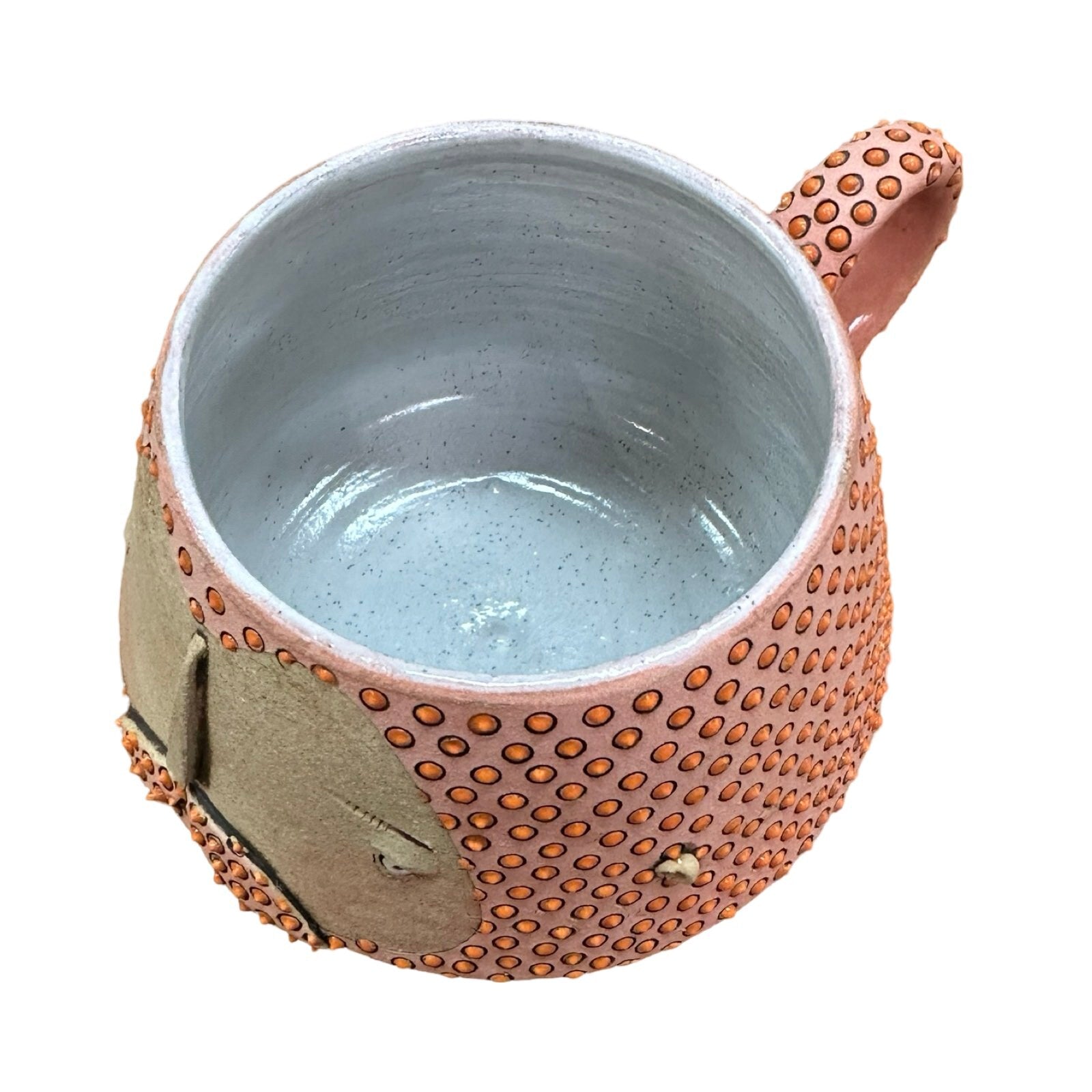 A handmade ceramic mug with a carved man's face and moustache, glazed in pink with a red diamond design.
