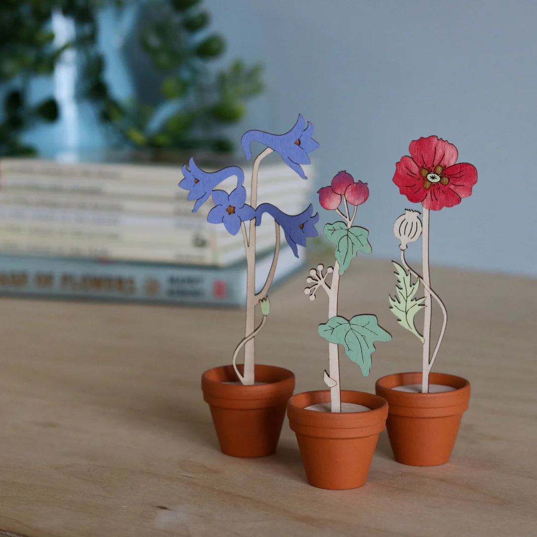 Decorative wooden flowers in terracotta pots on a wooden surface with blurred books in the background.