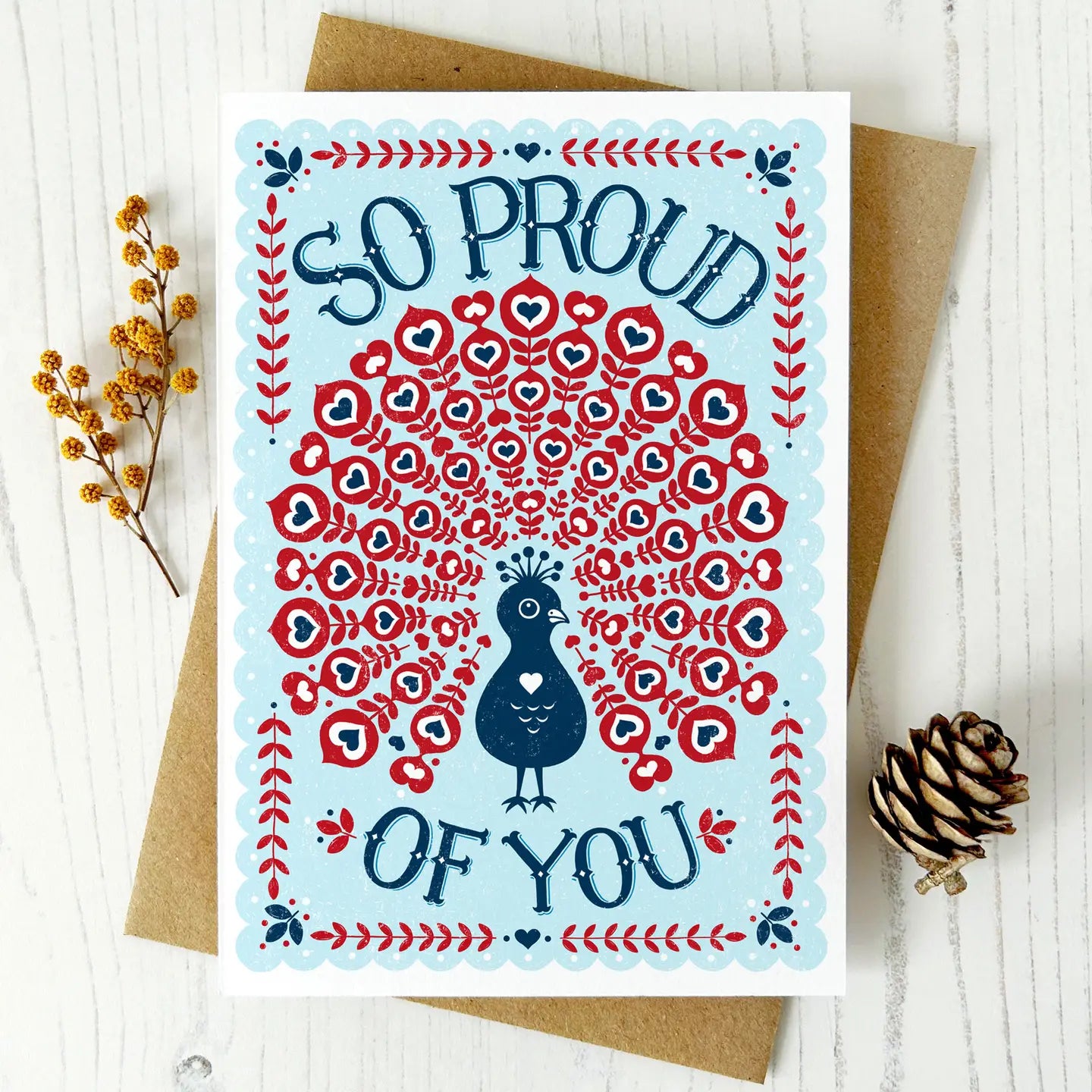 Greeting card with peacock design and 'So Proud of You' text on a white background.