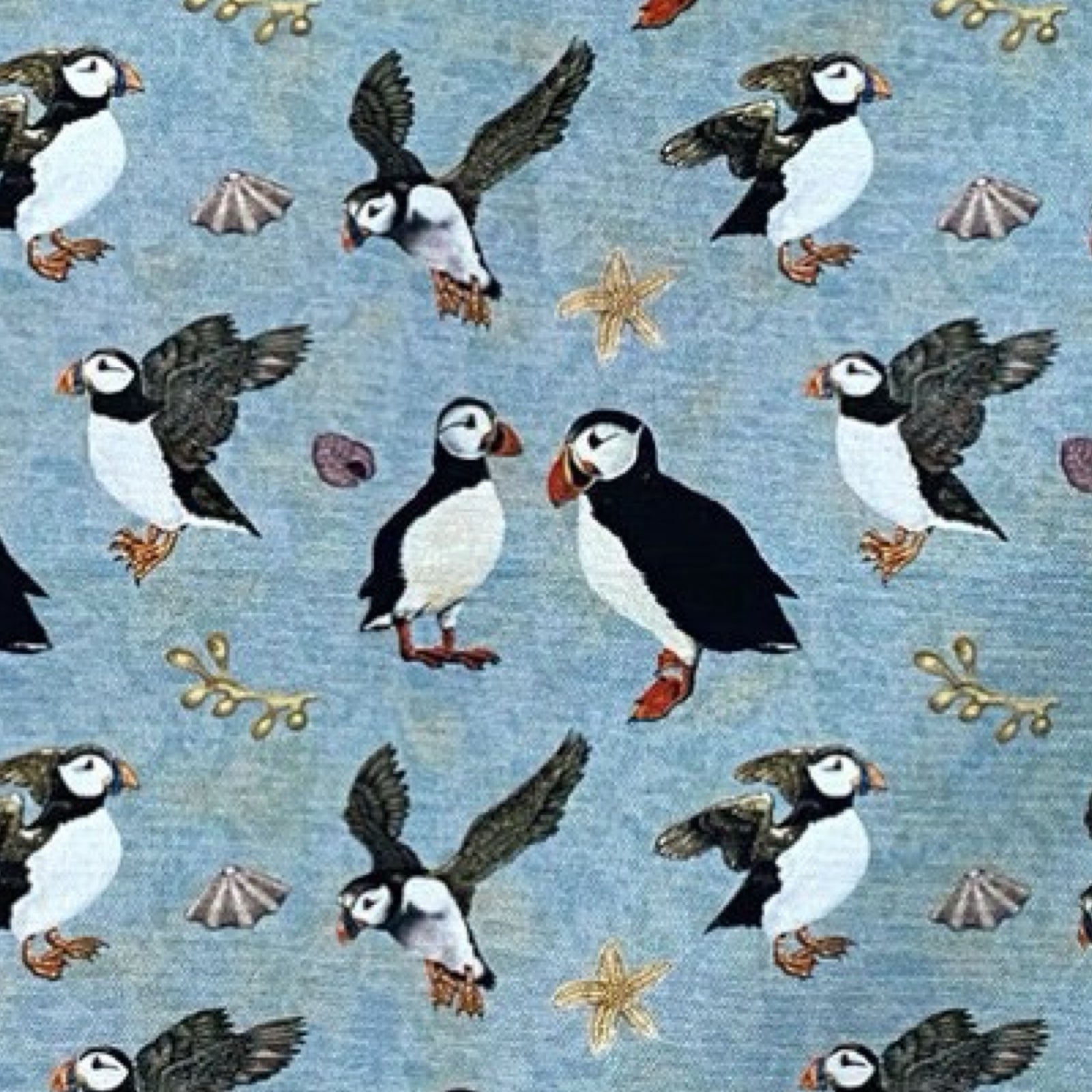 A tea towel featuring illustrations of standing and flying puffins against a blue / green background.
