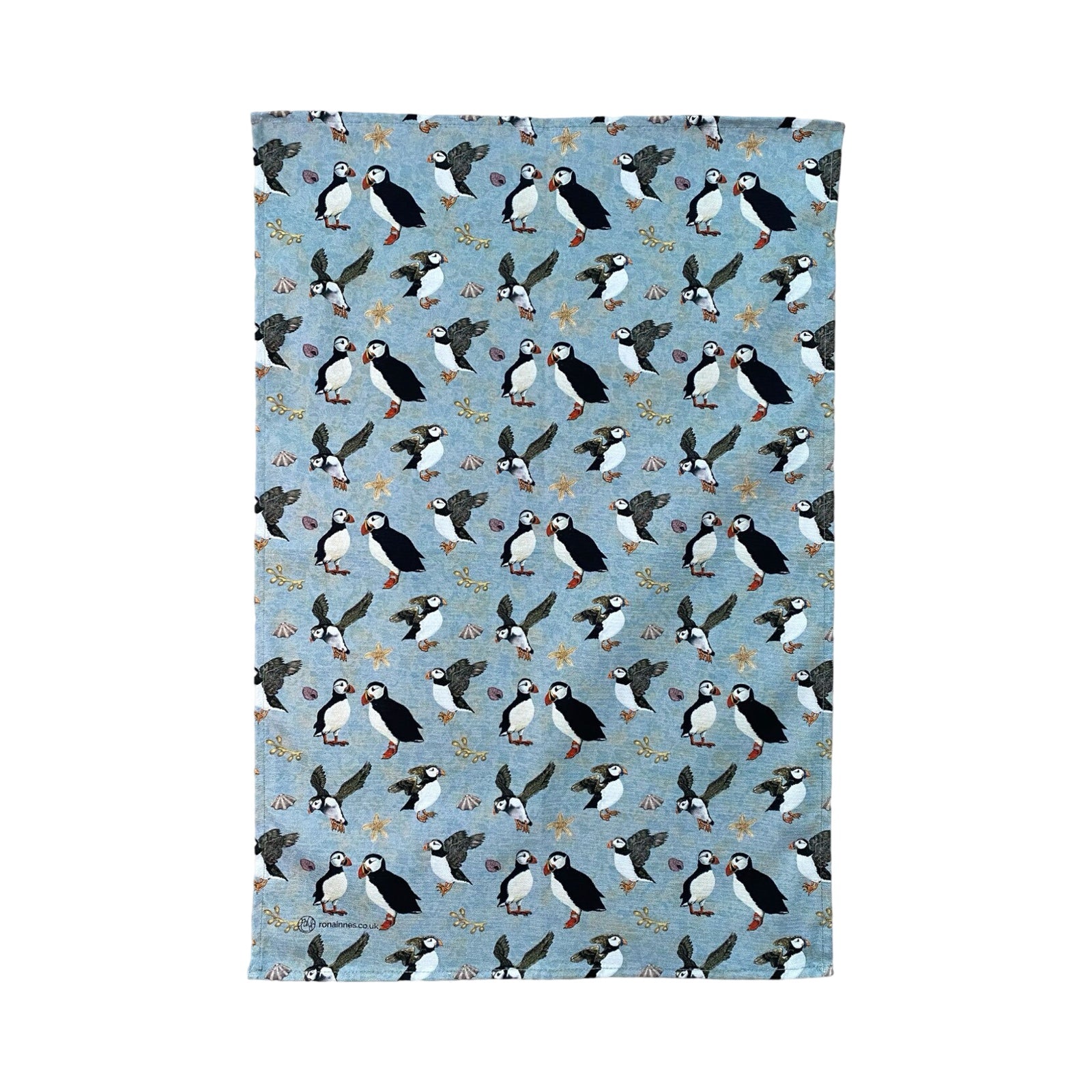 A tea towel featuring illustrations of standing and flying puffins against a blue / green background.