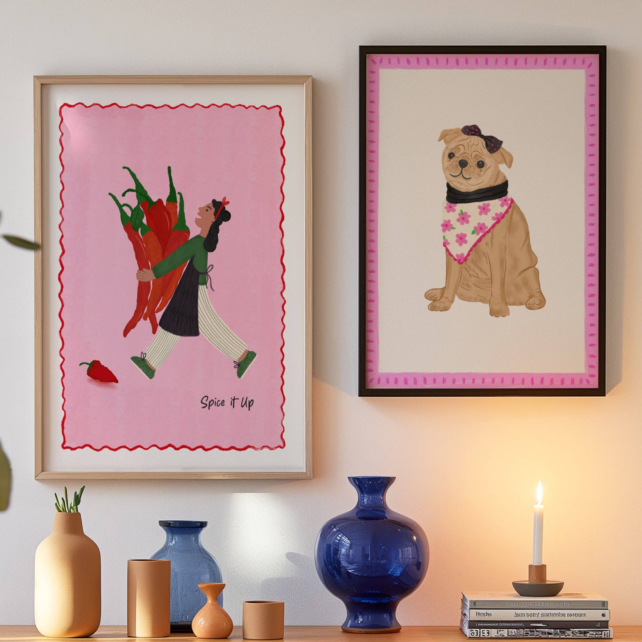 Illustration of a dog wearing a bandana in a pink frame, in a black frame next to another framed art print hung up on a wall.