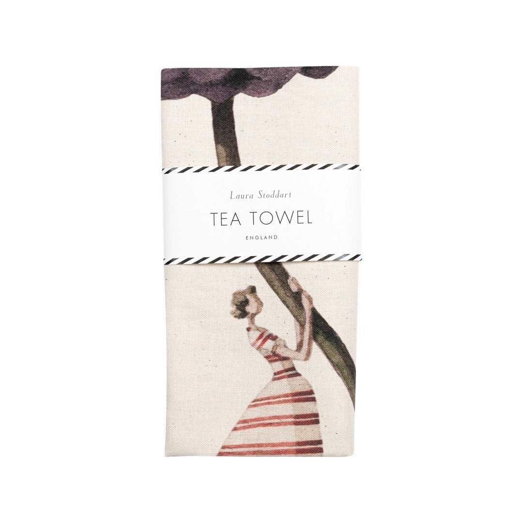 A folded floral tea towel featuring an illustration of a lady holding a giant purple dahlia flower.