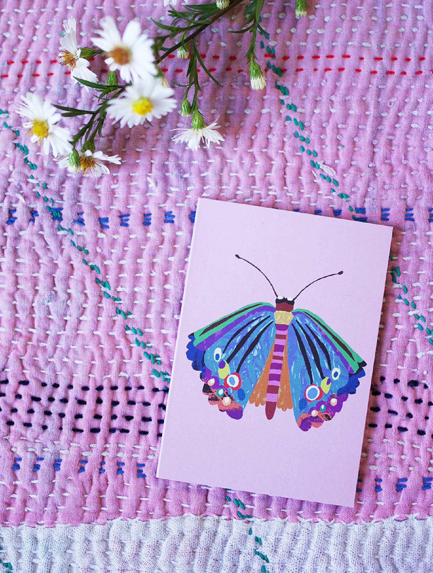 Colourful butterfly card on a textured pink surface with flowers.