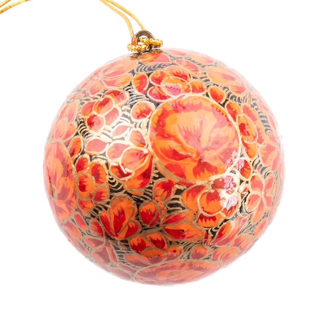 A round papier mache bauble in black with a gold and red floral design.