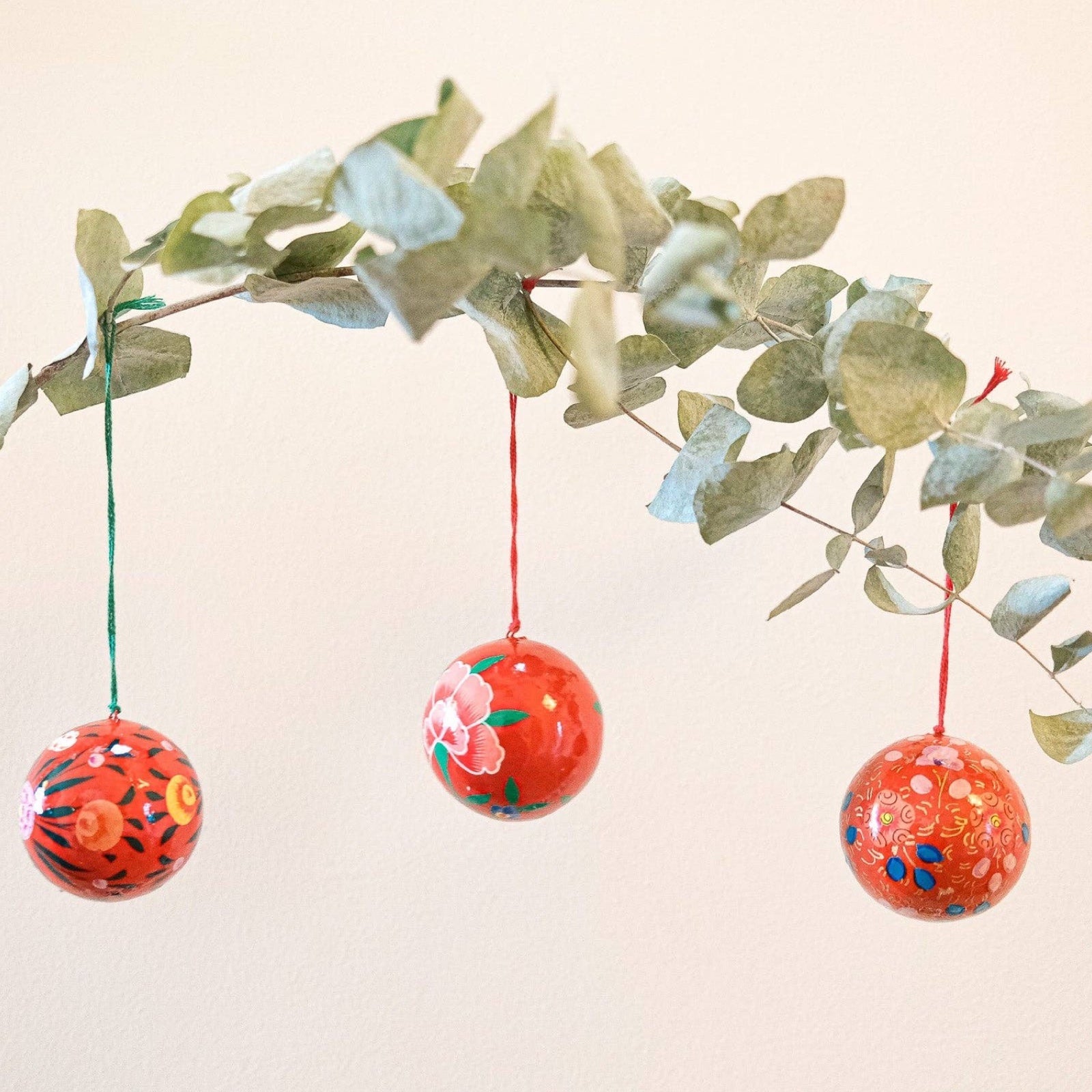 3 round red Christmas baubles hanging from a branch.