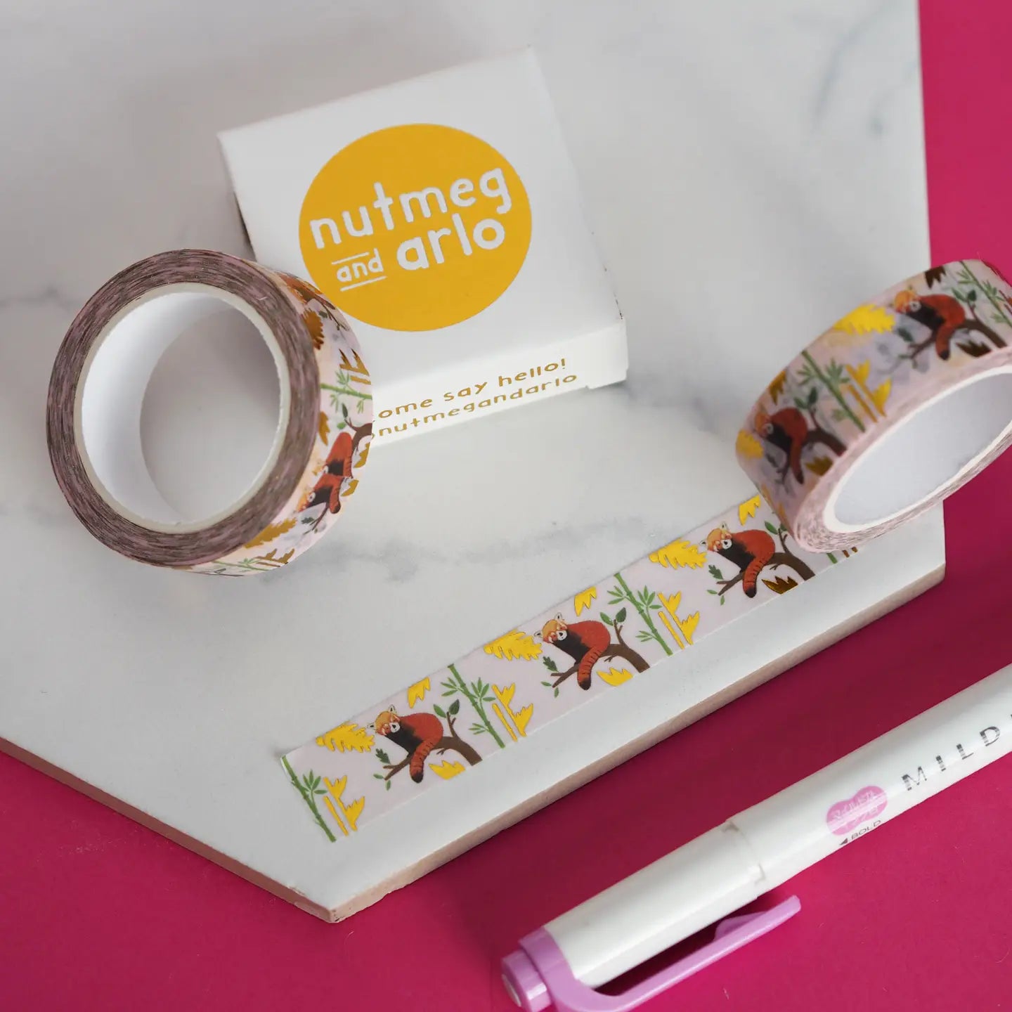 Decorative tape with cartoon pandas and 'nutmeg and arlo' branding on a pink surface.