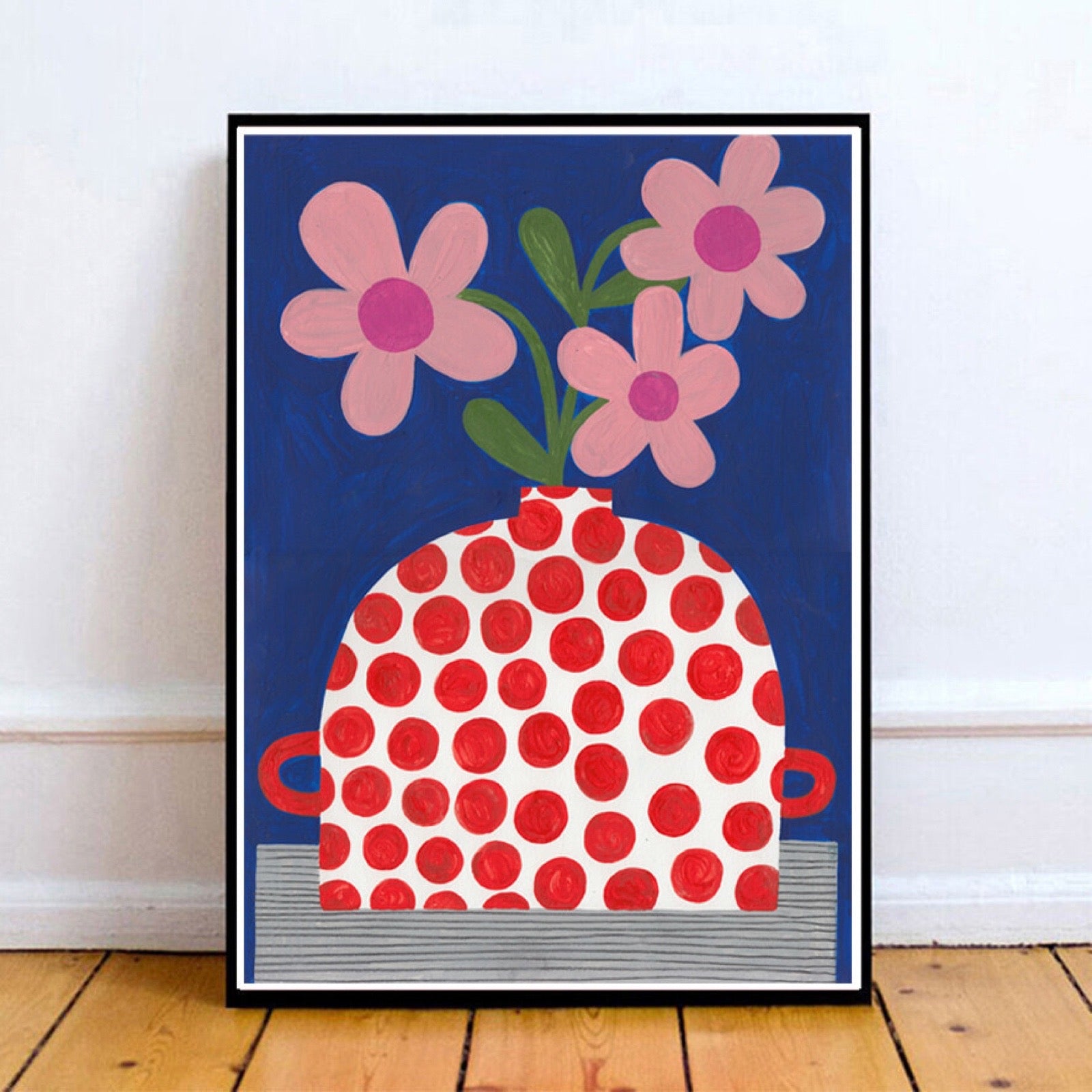Framed artwork of a red polka dot vase with pink flowers on a blue background.