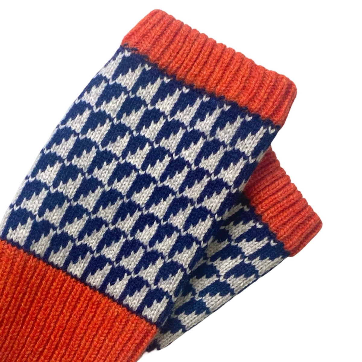 A close-up of a knit wrist warmers featuring a navy blue and off-white pattern with bright orange ribbed trim.