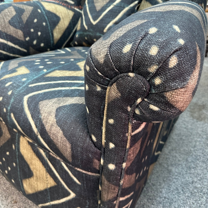 Close-up of an upholstered armchair corner with a dark abstract patterned fabric in charcoal, black, and beige, resting on a grey carpet.